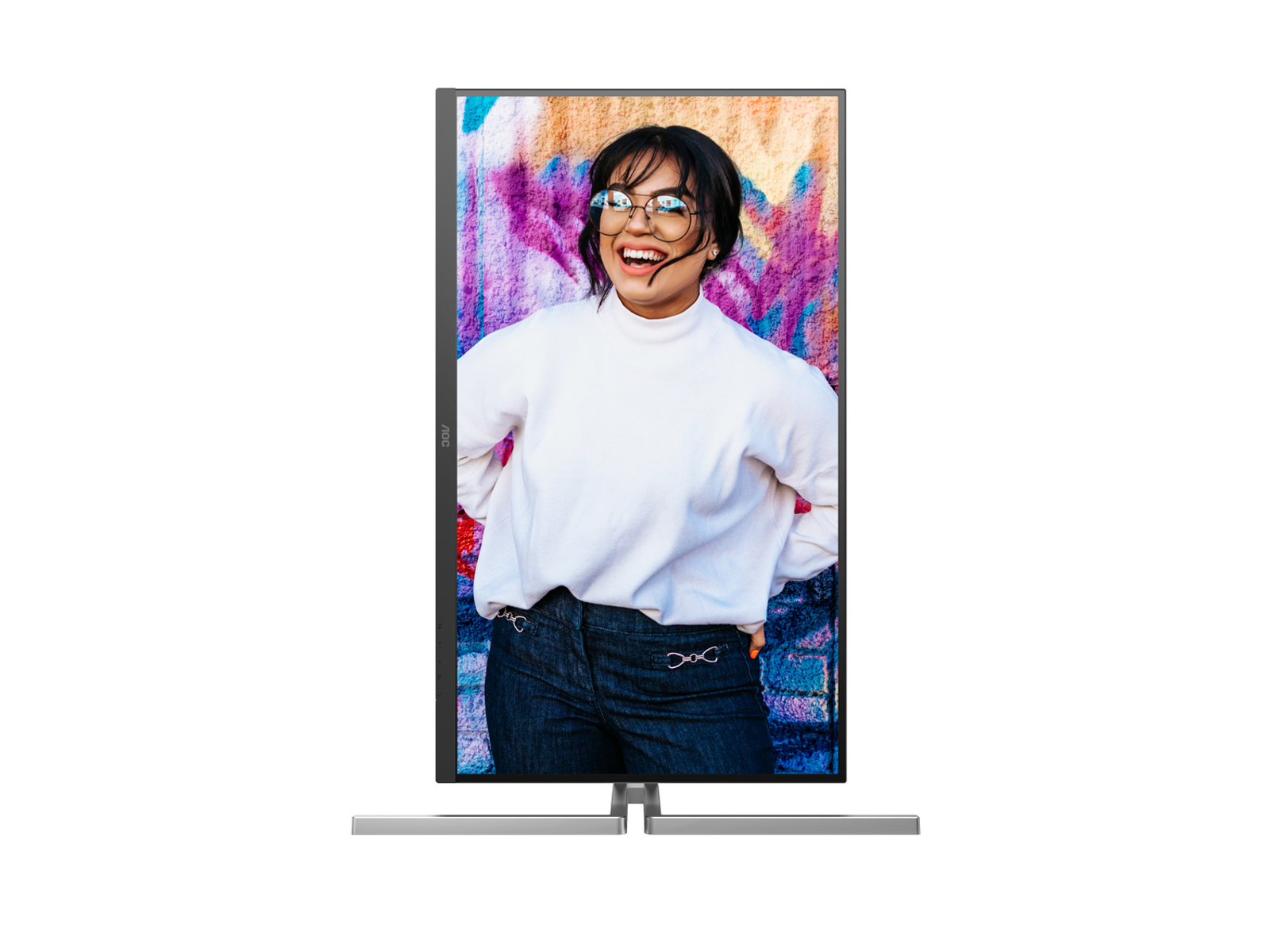 Kobieta w okularach uśmiecha się przed kolorową ścianą. Ma na sobie biały sweter i dżinsy, wyświetlane na ekranie komputera.