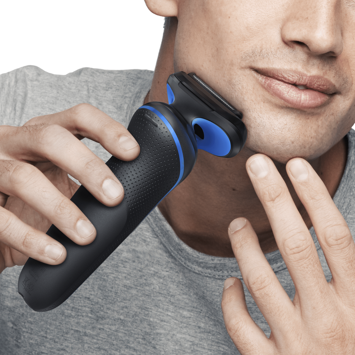 Un uomo si rade il viso con un rasoio elettrico. Il rasoio è nero e blu. Indossa una maglietta grigia.