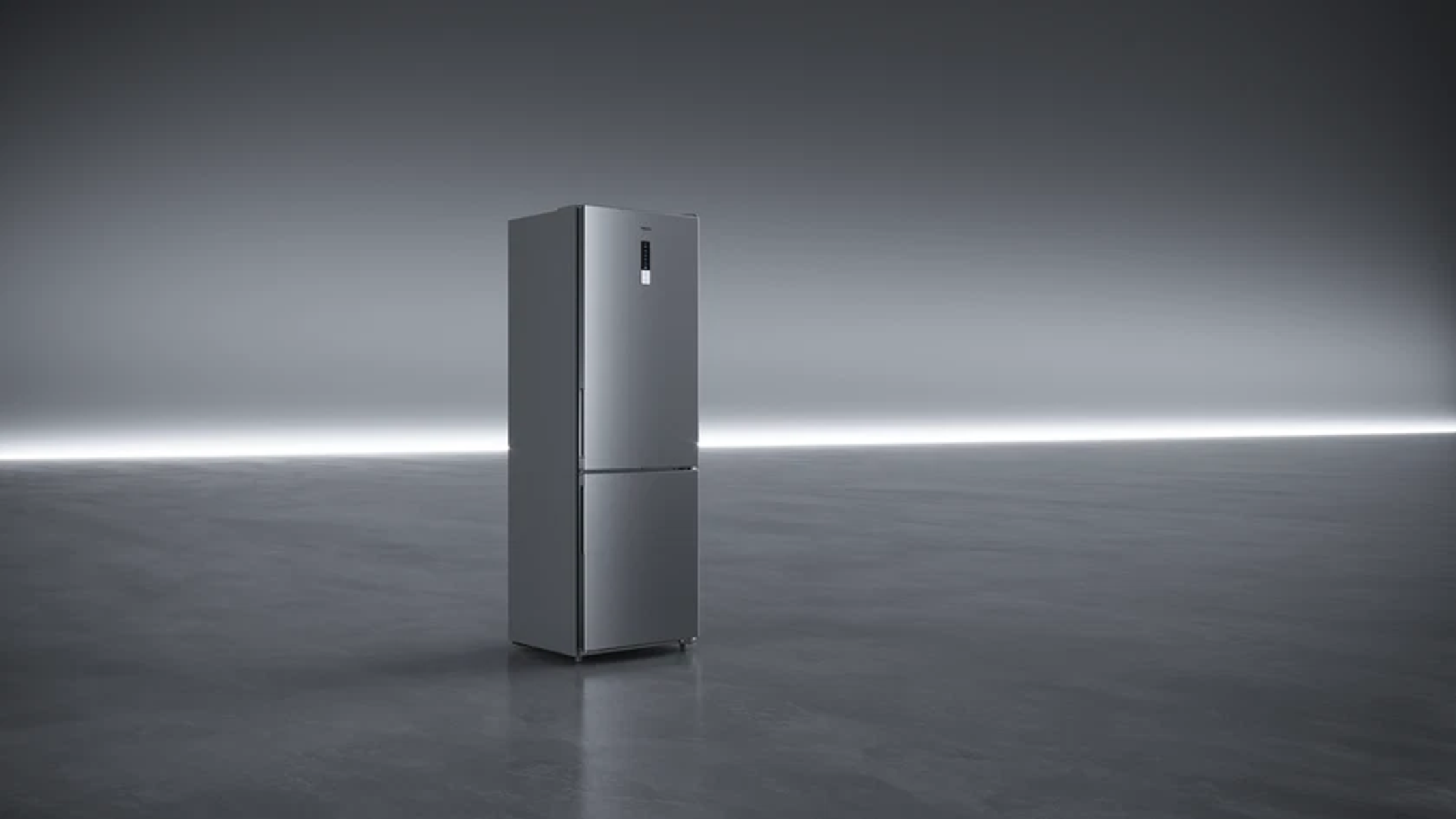 Un frigorífico moderno y plateado está sobre un suelo gris reflectante. El fondo es un degradado gris, con luz horizontal brillante.