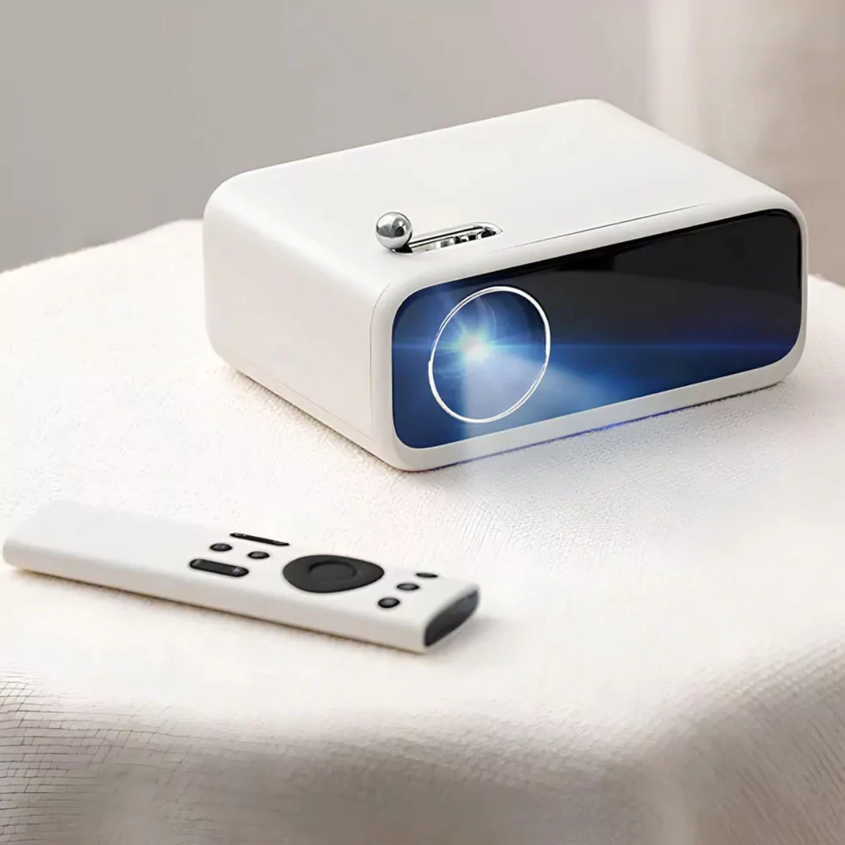 Un proyector blanco con lente brillante sobre una superficie blanca. Un mando a distancia blanco está delante.