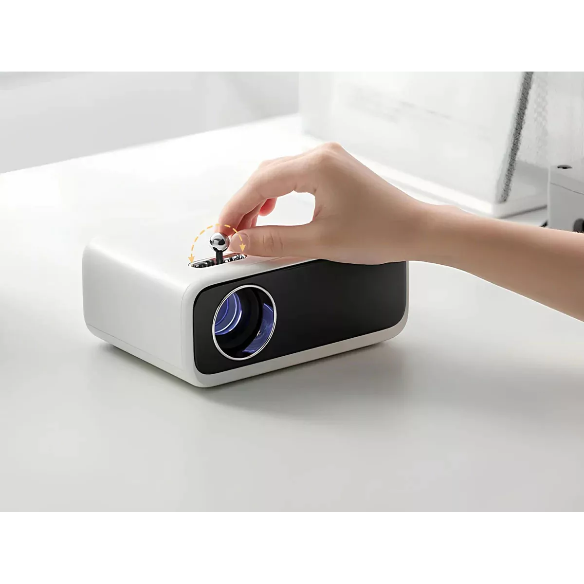 Una persona ajusta un proyector blanco y negro sobre una superficie blanca. La mano de la persona gira una perilla de control en la parte superior del dispositivo.