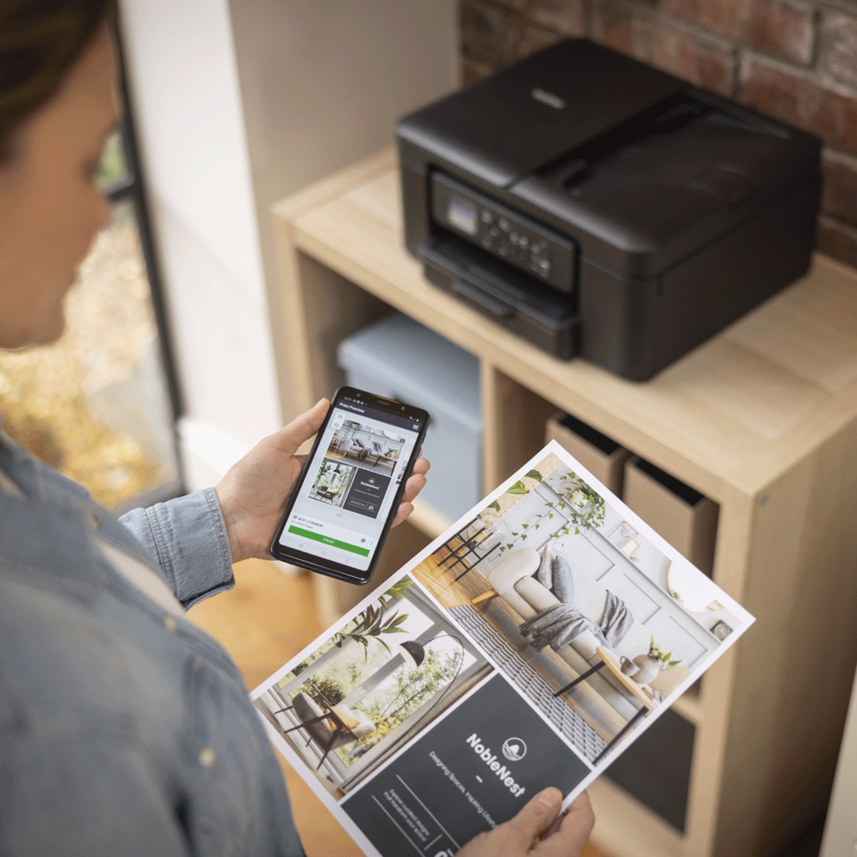 Kobieta trzyma telefon i broszurę, drukarka na półce. Broszura pokazuje obrazy projektów wnętrz.
