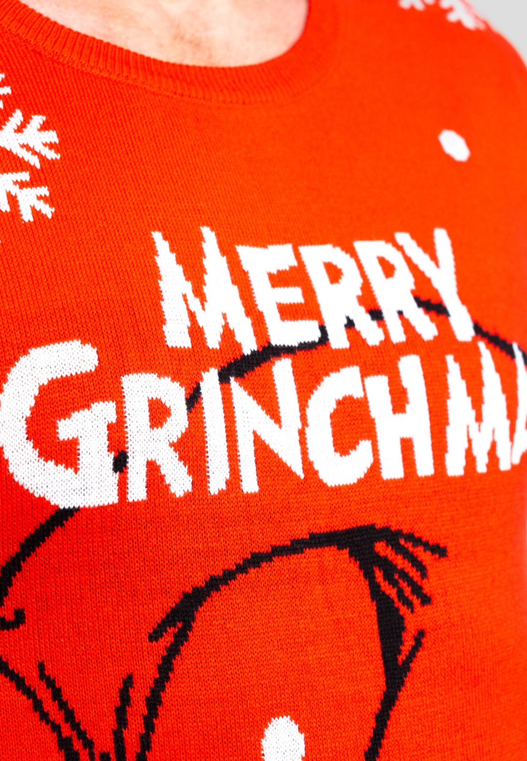 Orangener Pullover mit weißem Schriftzug 'Merry Grinchmas' und Grinch-Gesicht. Schneeflocken sind sichtbar. Person trägt Pullover.
