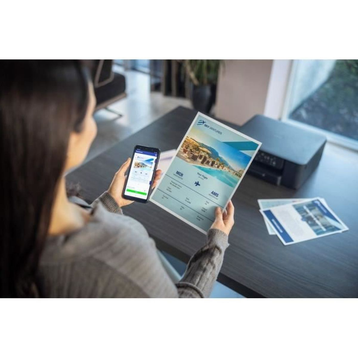 Kobieta trzyma telefon i wydrukowany dokument ze szczegółami lotu. Na stole drukarka i inne papiery. Scena ma miejsce w pomieszczeniu.