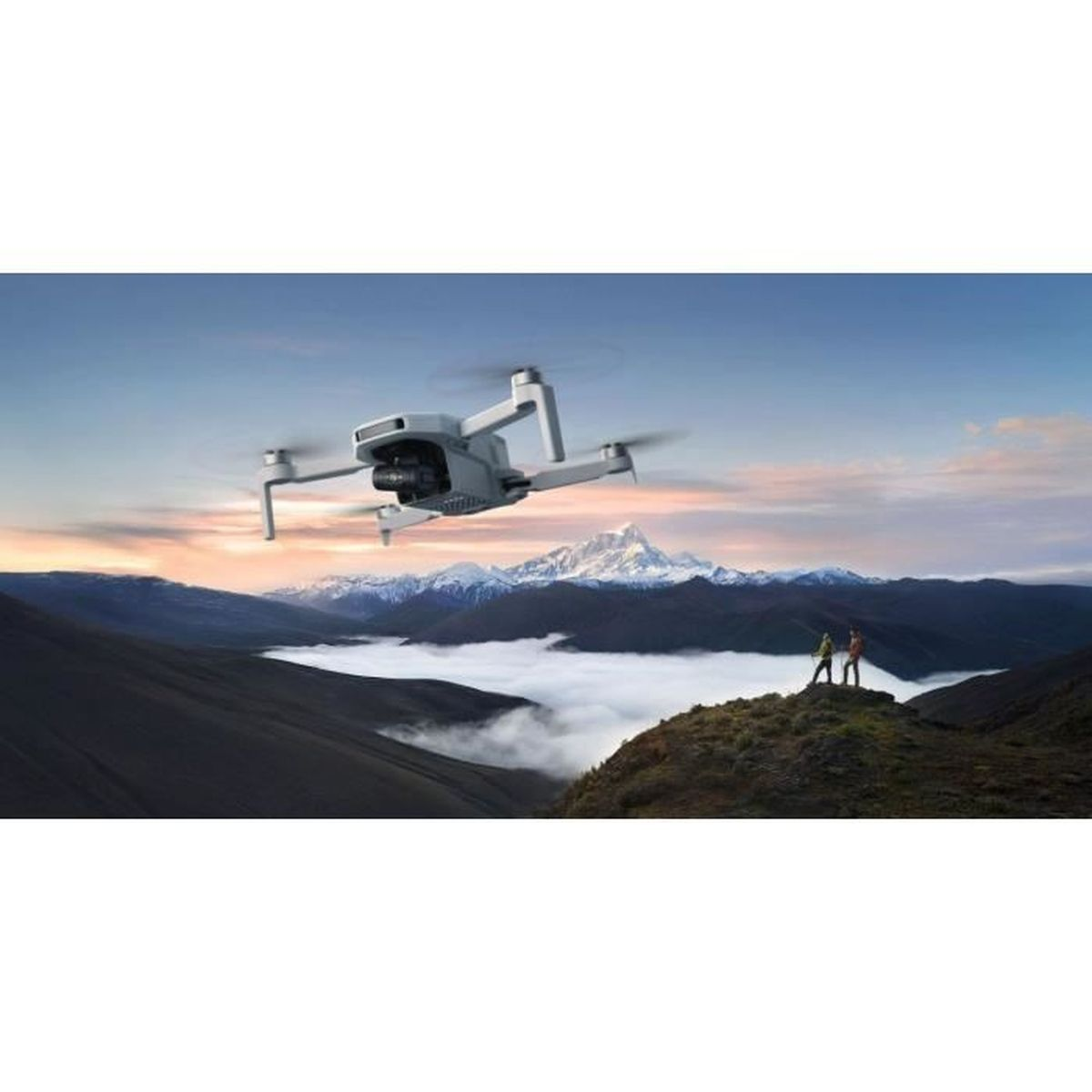 Dron leci nad górskim krajobrazem, z dwiema osobami na wzgórzu. Tło wypełniają góry i chmury.