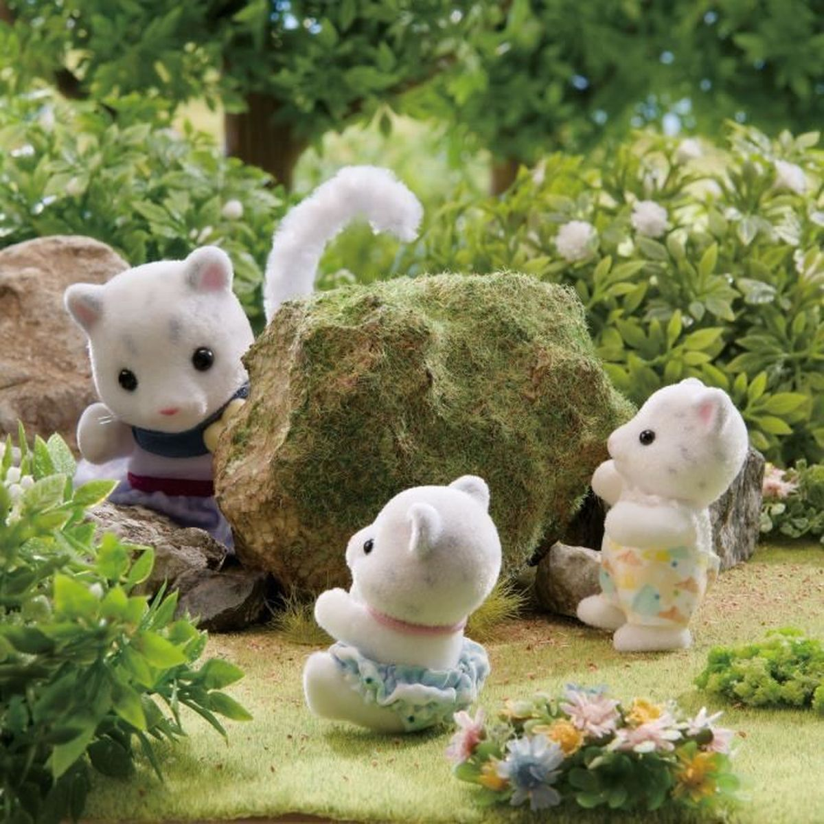 Tres figuras de osos blancos en un jardín. Están cerca de una roca cubierta de musgo, rodeadas de vegetación y flores coloridas.
