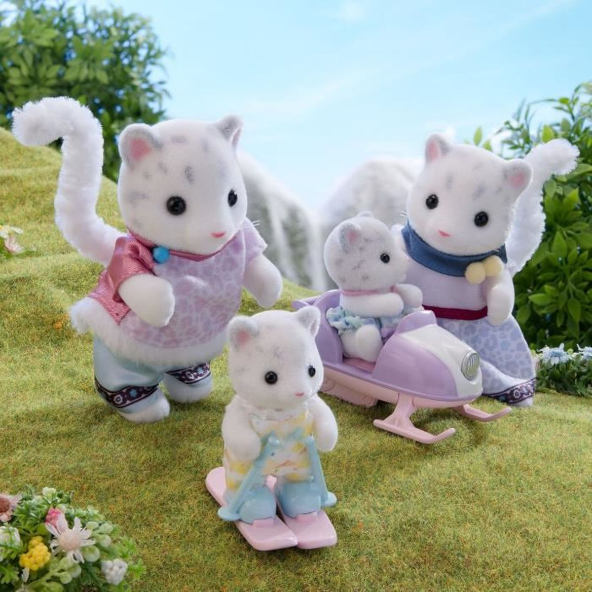 Cuatro figuras de gatos blancos con trajes coloridos. Uno con esquís, otro en un vehículo y dos de pie sobre hierba verde con un macizo de flores.