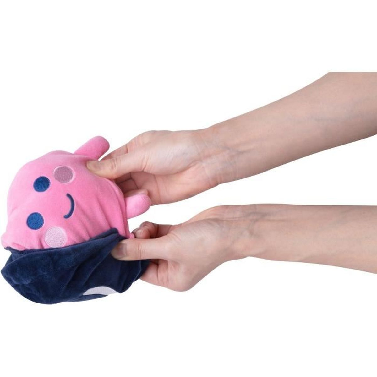 Mains tenant un jouet en peluche rose avec des détails bleus et roses, et une base bleu foncé. Le jouet ressemble à un personnage.
