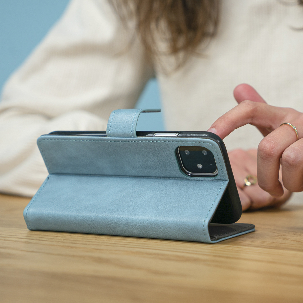 La mano di una persona tocca una custodia blu per telefono su un tavolo di legno. La custodia è aperta, rivelando la fotocamera del telefono.
