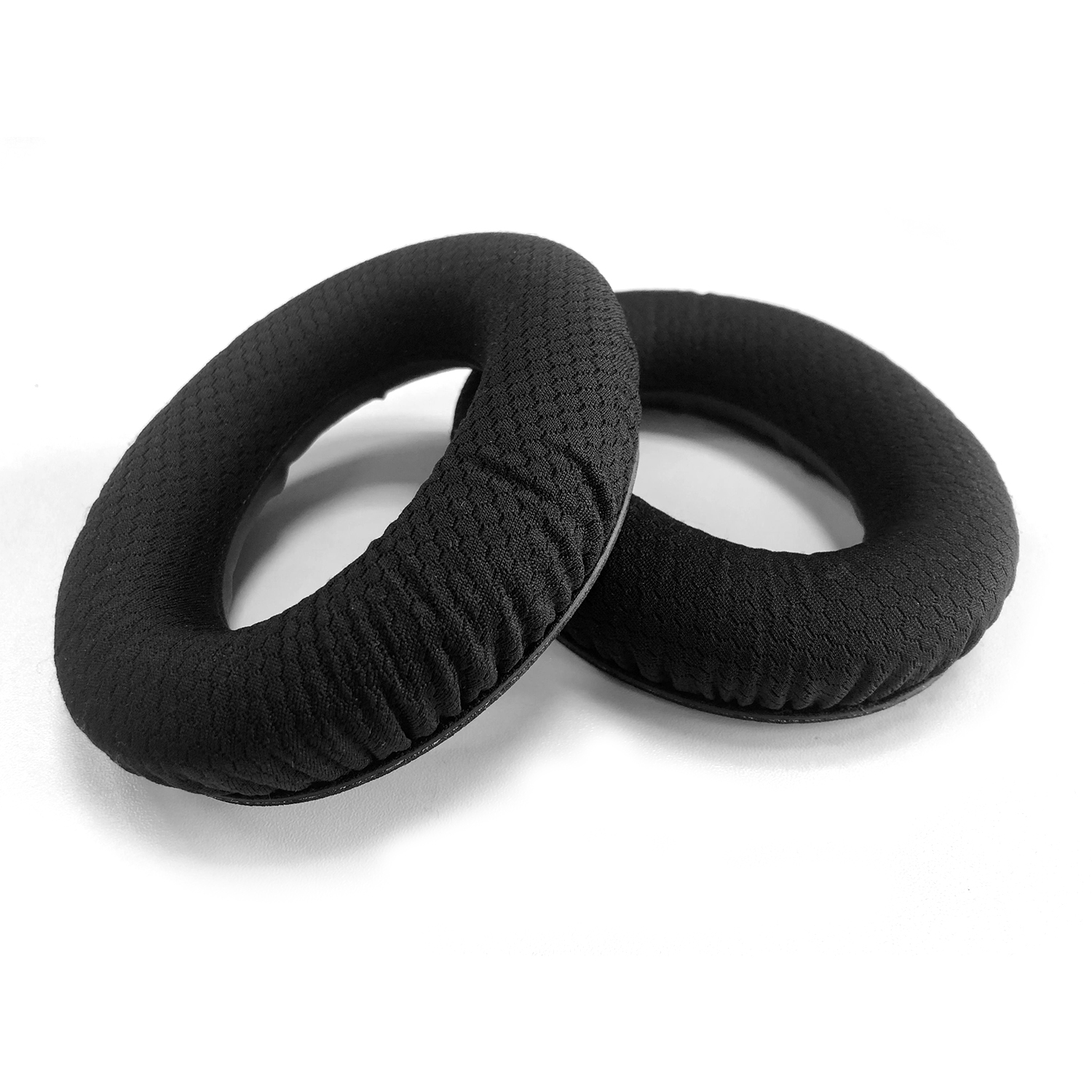 Dwie czarne poduszki w kształcie pierścienia do słuchawek na białej powierzchni. Poduszki są wykonane z teksturowanej tkaniny.