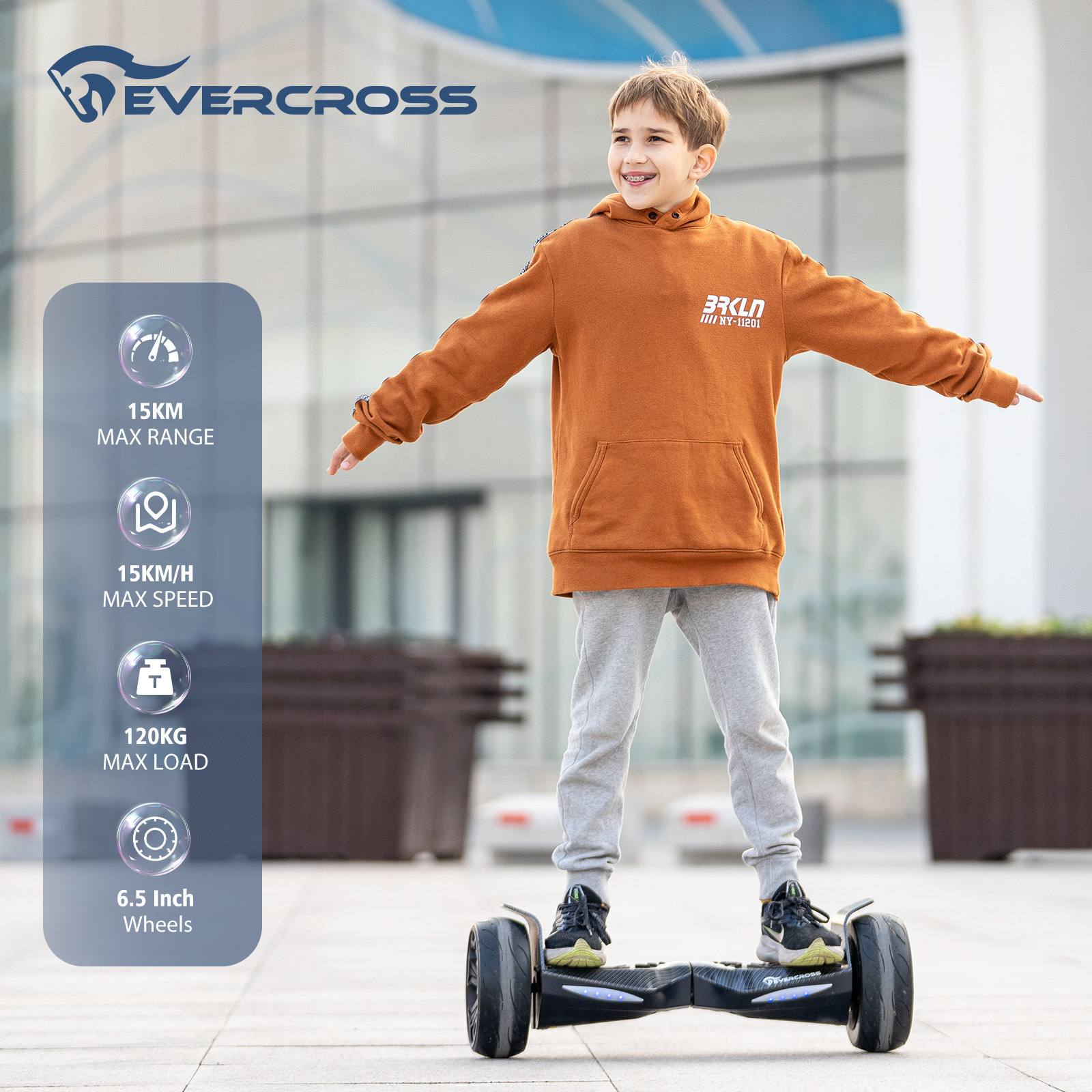 A boy on a hoverboard smiles. He wears an orange hoodie and gray pants. The hoverboard is black. Background shows info graphics.
