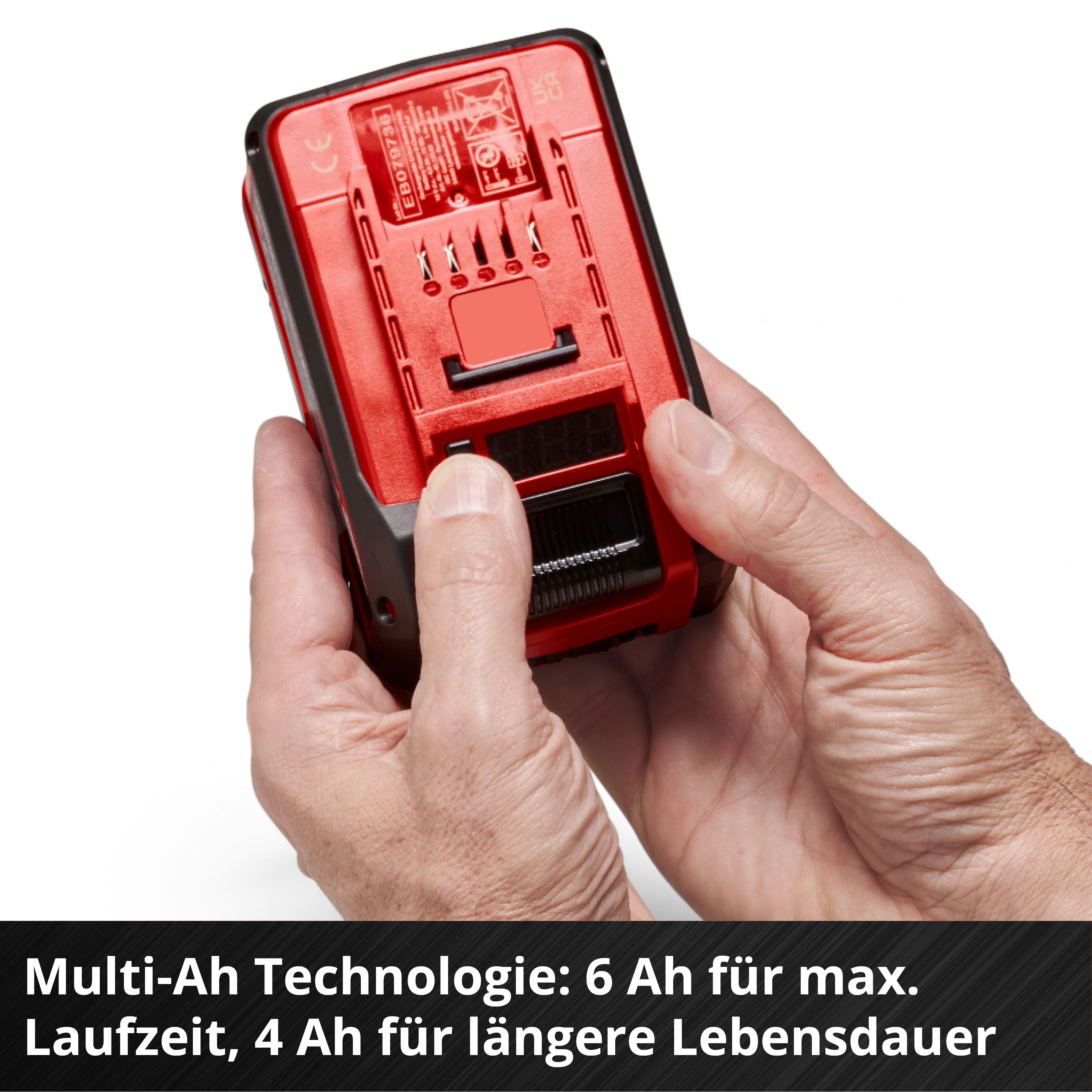 Una batteria rossa e nera per utensili elettrici è tenuta da due mani su sfondo bianco. Un display digitale è visibile.