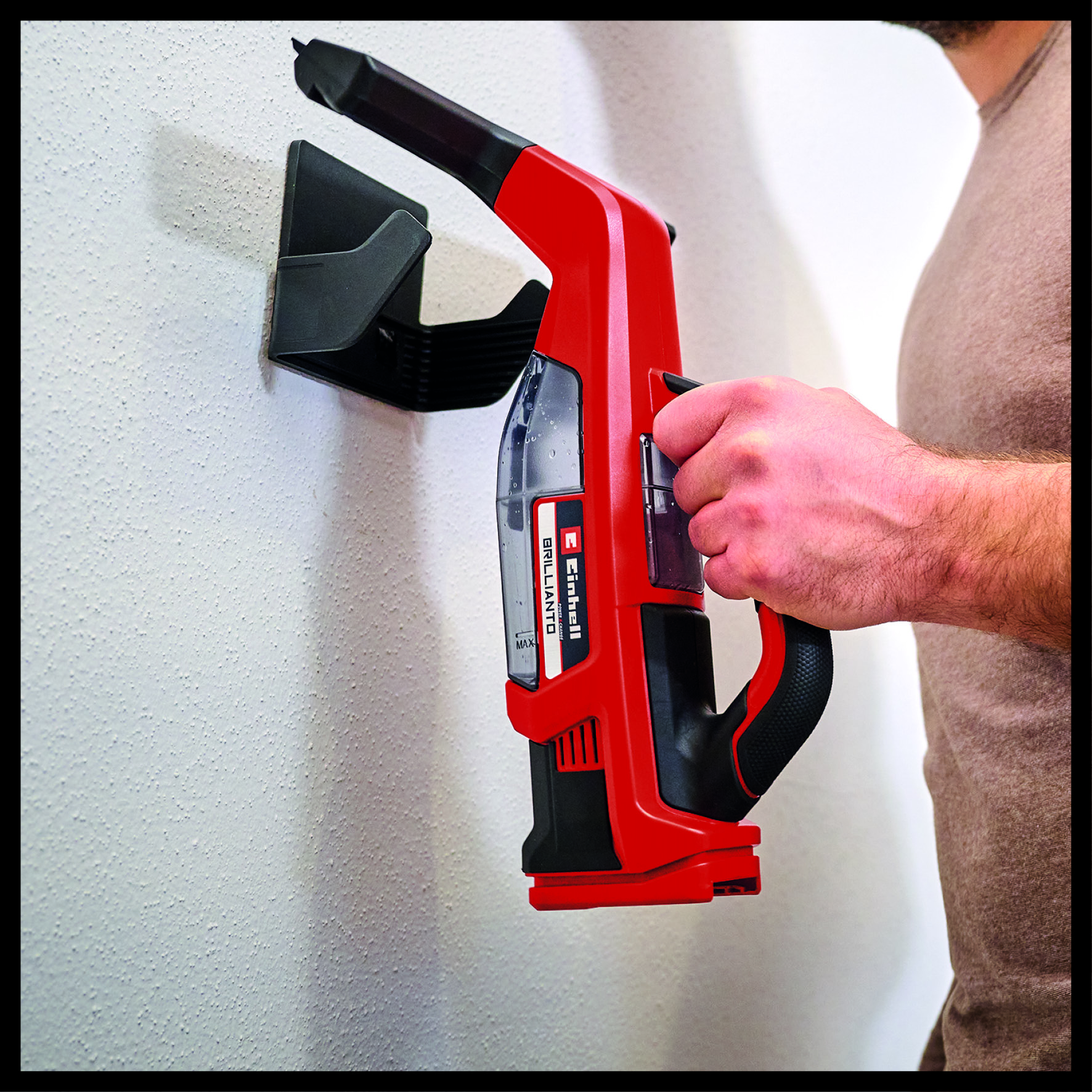 Mężczyzna trzyma czerwony odkurzacz. Jest zamontowany na ścianie. Odkurzacz jest czarny i ma czarny uchwyt.