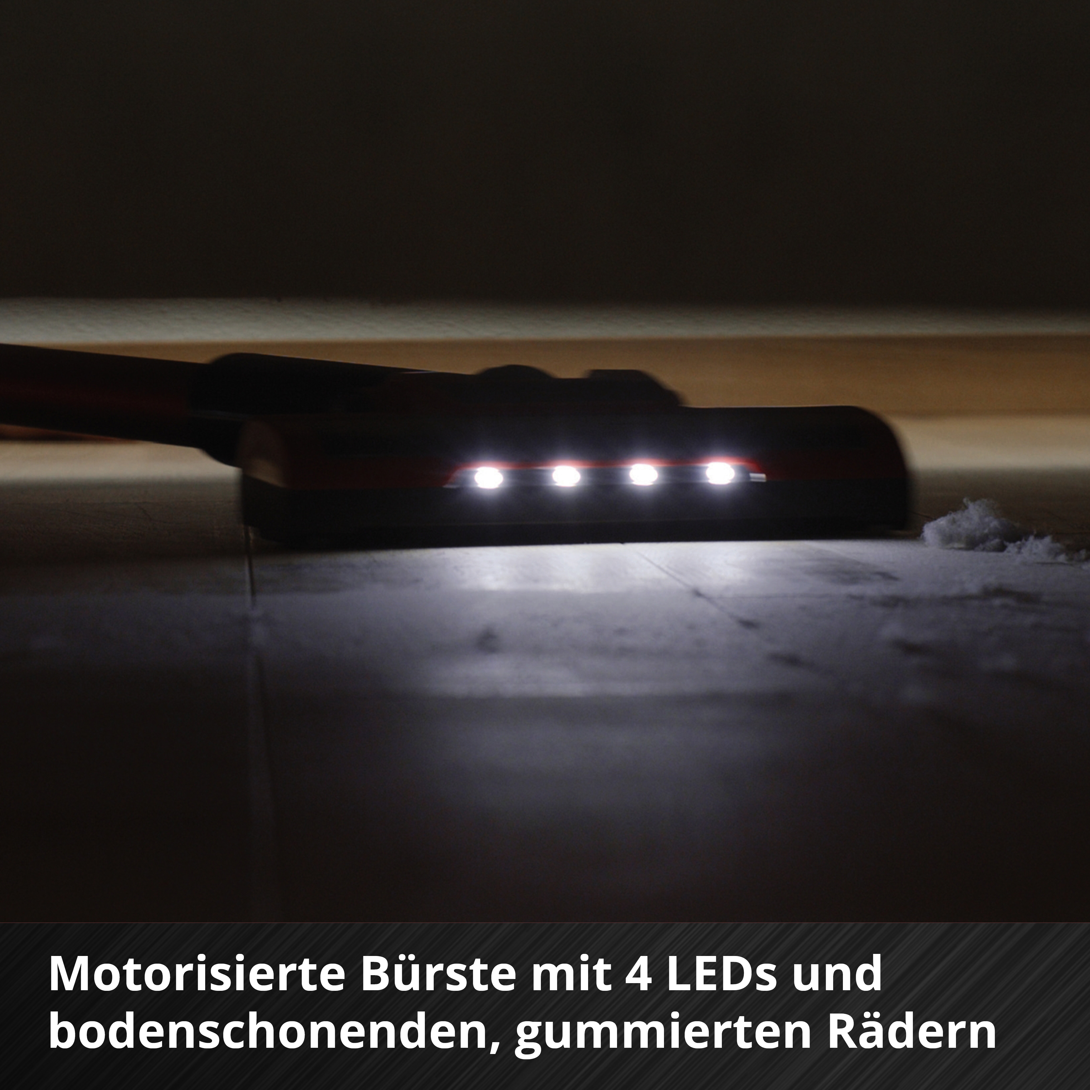 Una testina per aspirapolvere con 4 luci a LED sta pulendo un pavimento. Polvere visibile e spazio buio sotto un oggetto.