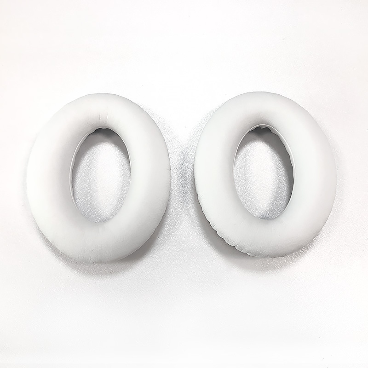 Dwie białe, okrągłe wkładki do słuchawek na białej powierzchni. Leżą obok siebie, pokazując wewnętrzny otwór i zewnętrzną poduszkę.