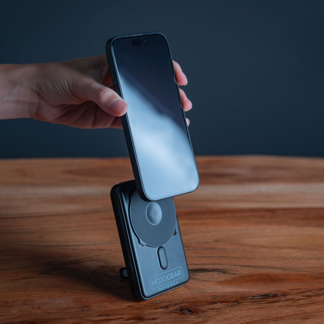 Eine Hand hält ein schwarzes Smartphone über einem schwarzen kabellosen Ladegerät auf einer Holzoberfläche, dunkler Hintergrund.