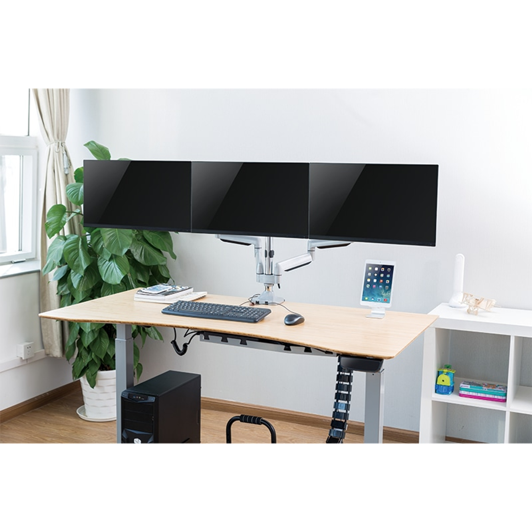 Ein Schreibtisch mit drei Monitoren, Tastatur, Maus und einem Tablet. Ein Computerturm steht darunter. Eine Pflanze und ein Regal sind ebenfalls vorhanden.