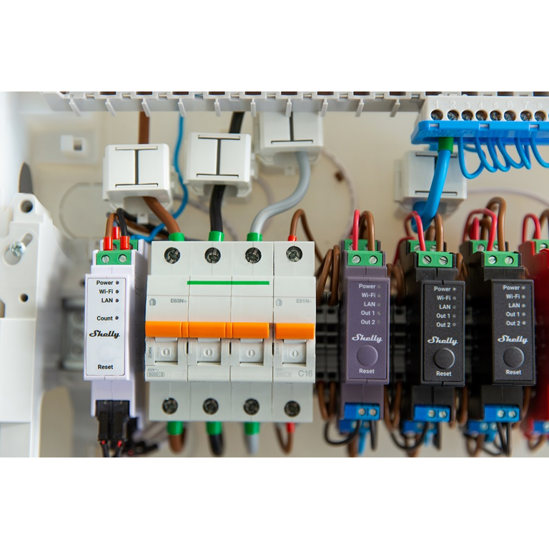 Panel elektryczny z wyłącznikami, okablowaniem i urządzeniami Shelly. Przewody są brązowe, niebieskie i czerwone. Scena jest dobrze oświetlona.
