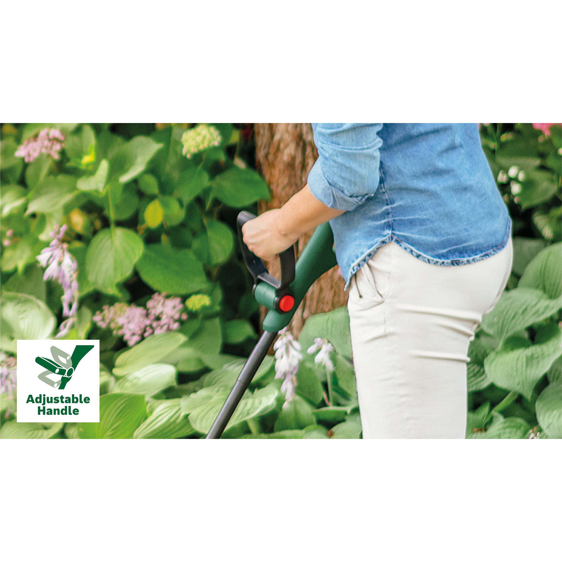 Eine Person in Jeans und weißer Hose hält ein grün-schwarzes Gartengerät zwischen grünen Blättern und lila Blumen.
