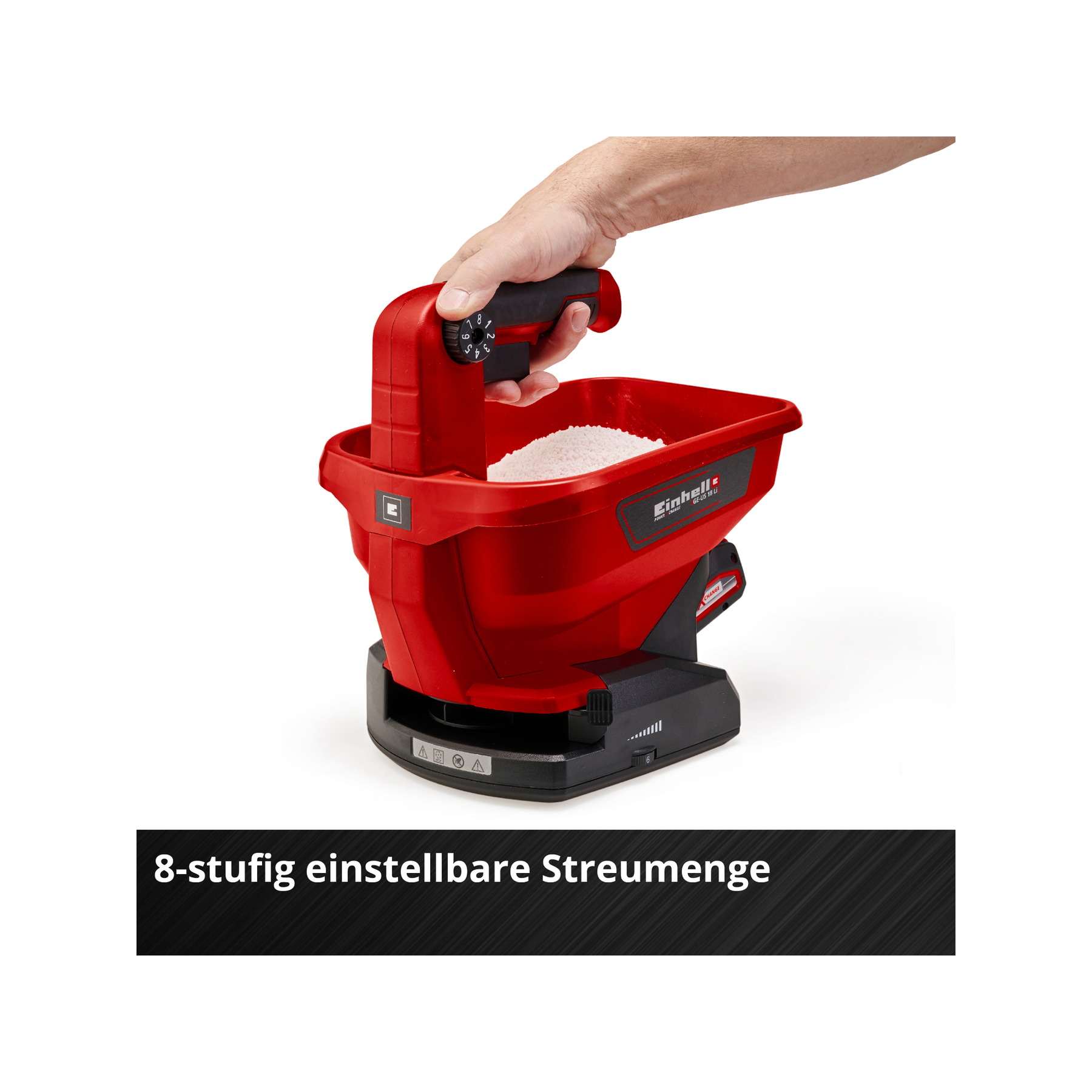 Czerwony rozsiewacz nawozu z dłonią trzymającą uchwyt. Ma pojemnik wypełniony białymi granulkami.