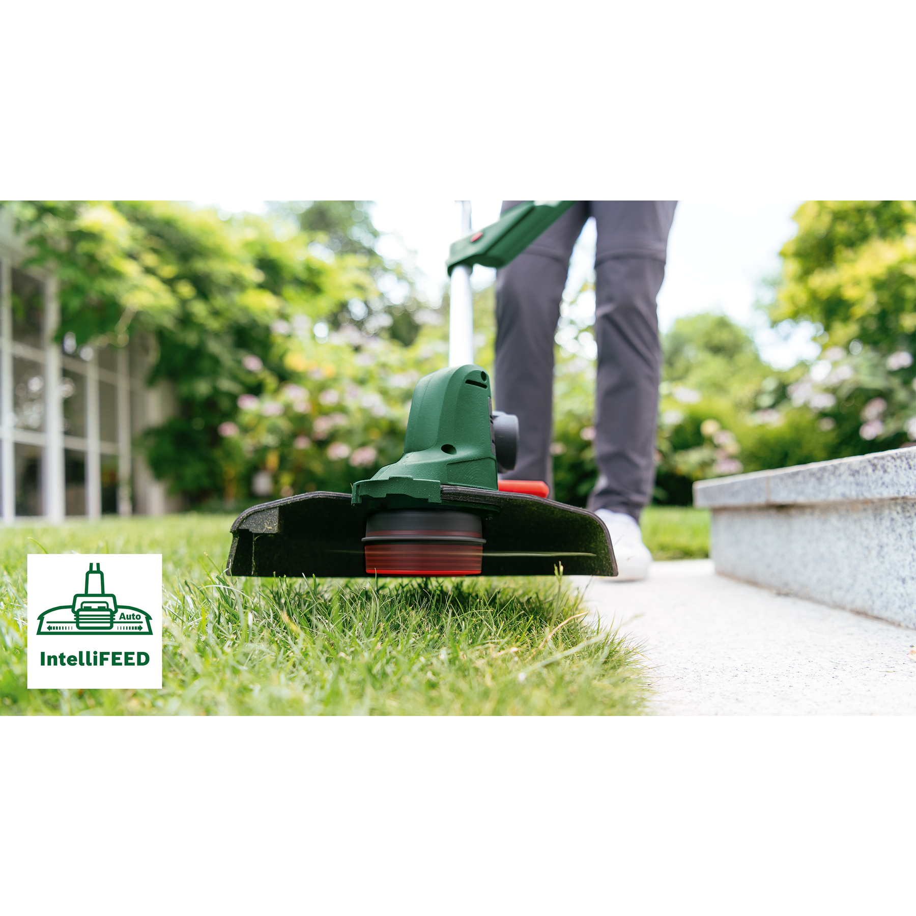 Eine Person benutzt einen grün-schwarzen Rasentrimmer auf einem Rasen. Der Hintergrund zeigt einen Garten mit grünen Pflanzen.