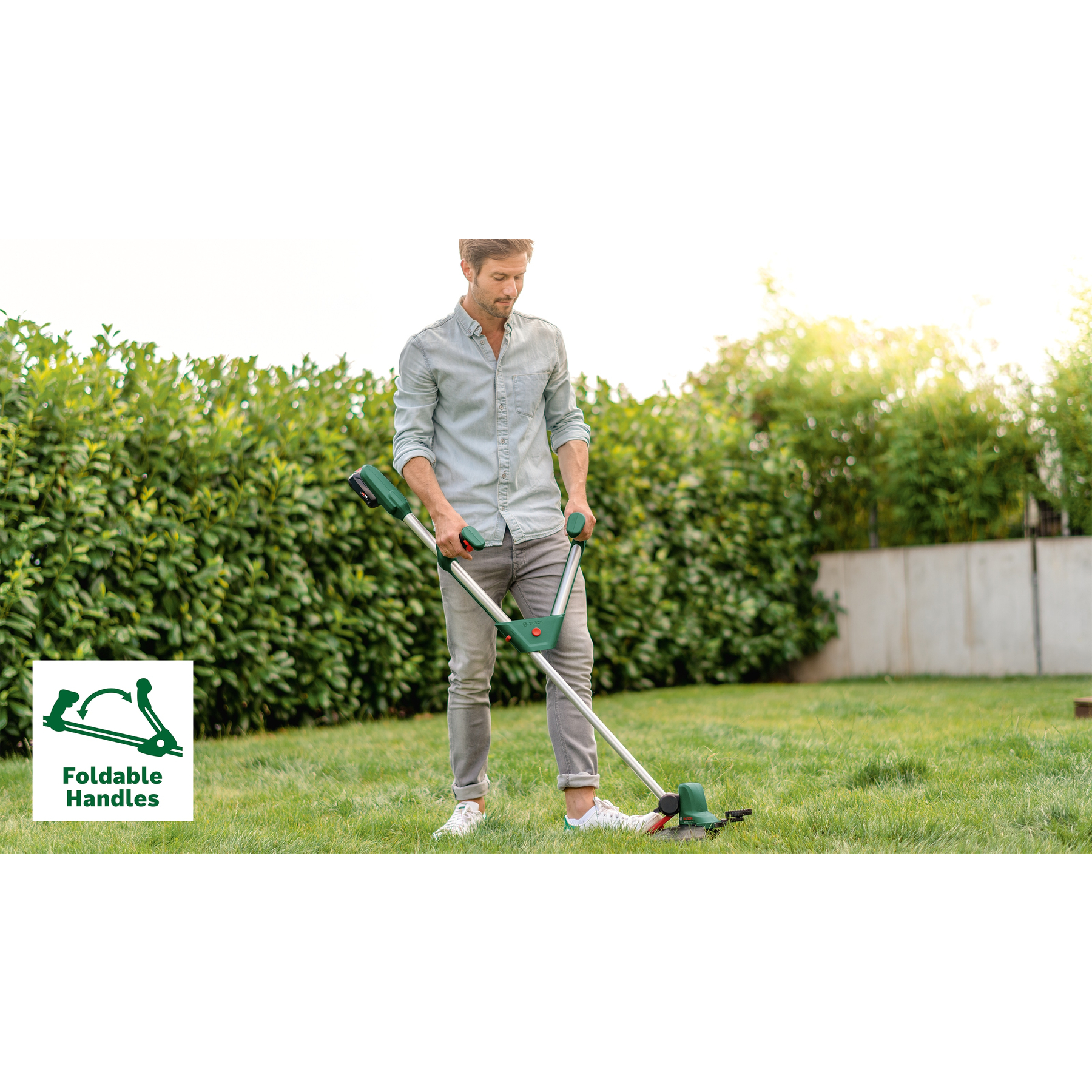 Ein Mann benutzt einen grünen und silbernen Rasenkantenabschneider auf einem grünen Rasen. Im Hintergrund befinden sich grüne Büsche.