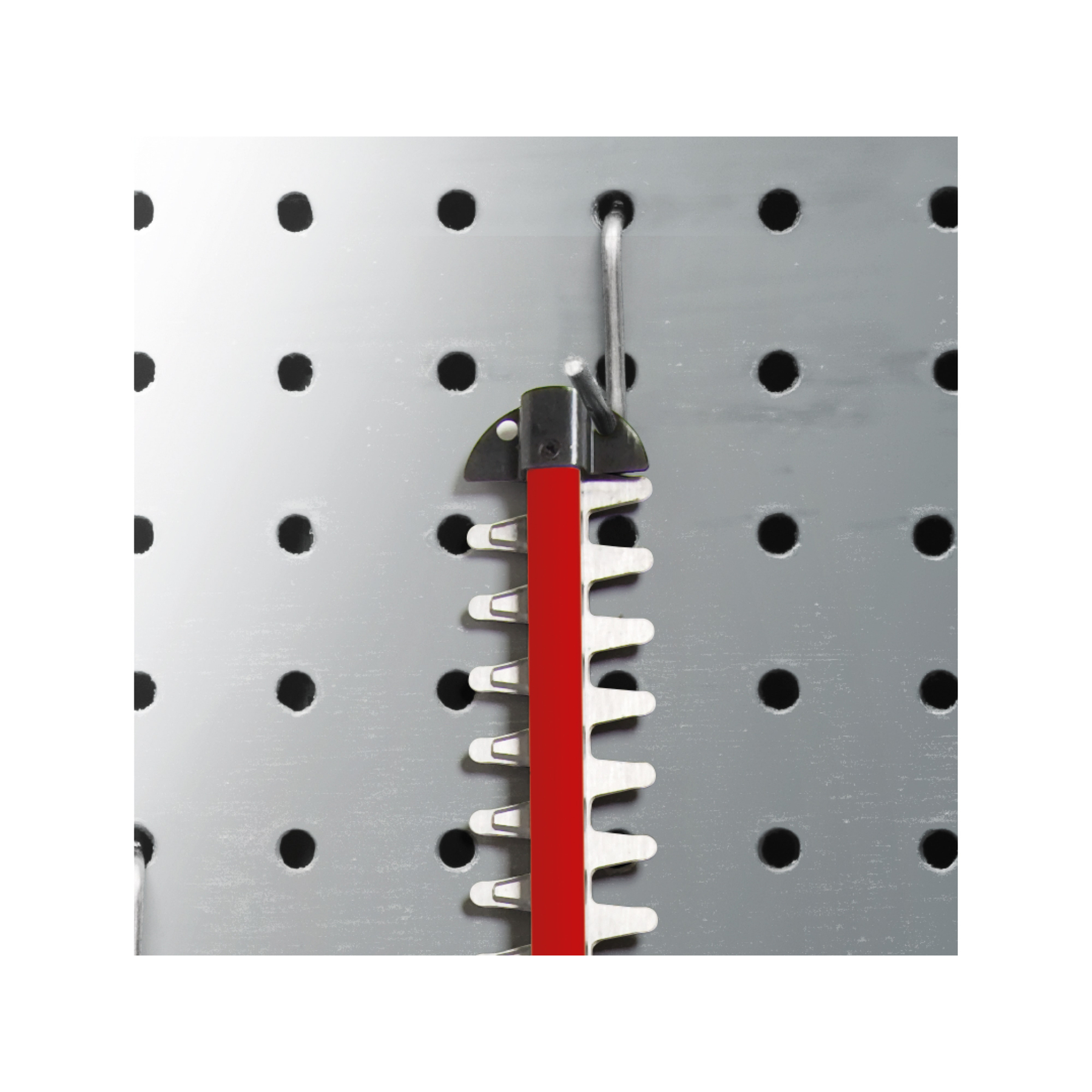 Eine Heckenscheren-Klinge hängt an einer Metall-Lochwand. Die Klinge ist rot, mit weißen Zähnen. Sie wird durch einen Metallhaken befestigt.