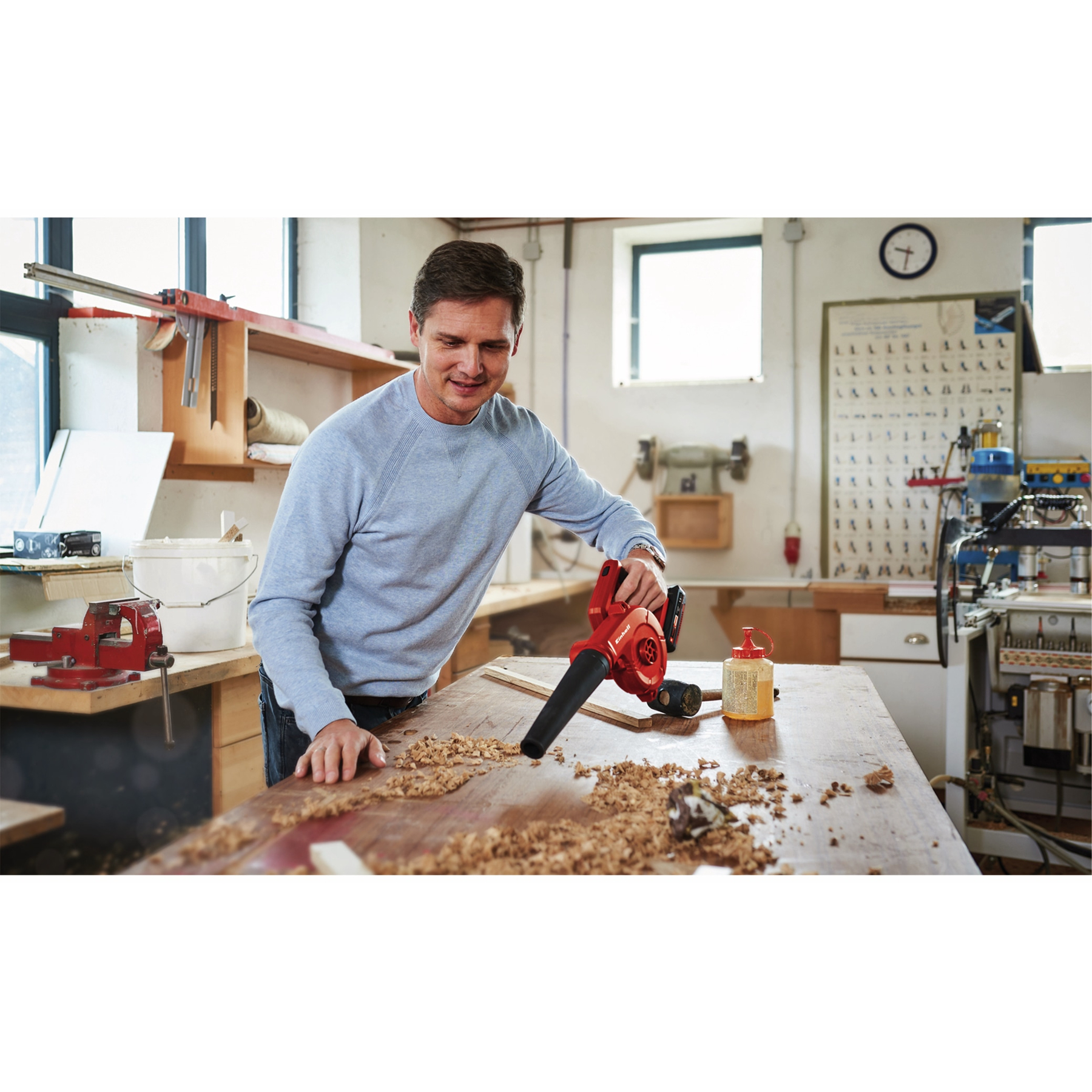 Mężczyzna używa czerwonej dmuchawy do liści na drewnianym stole z wiórami w warsztacie.