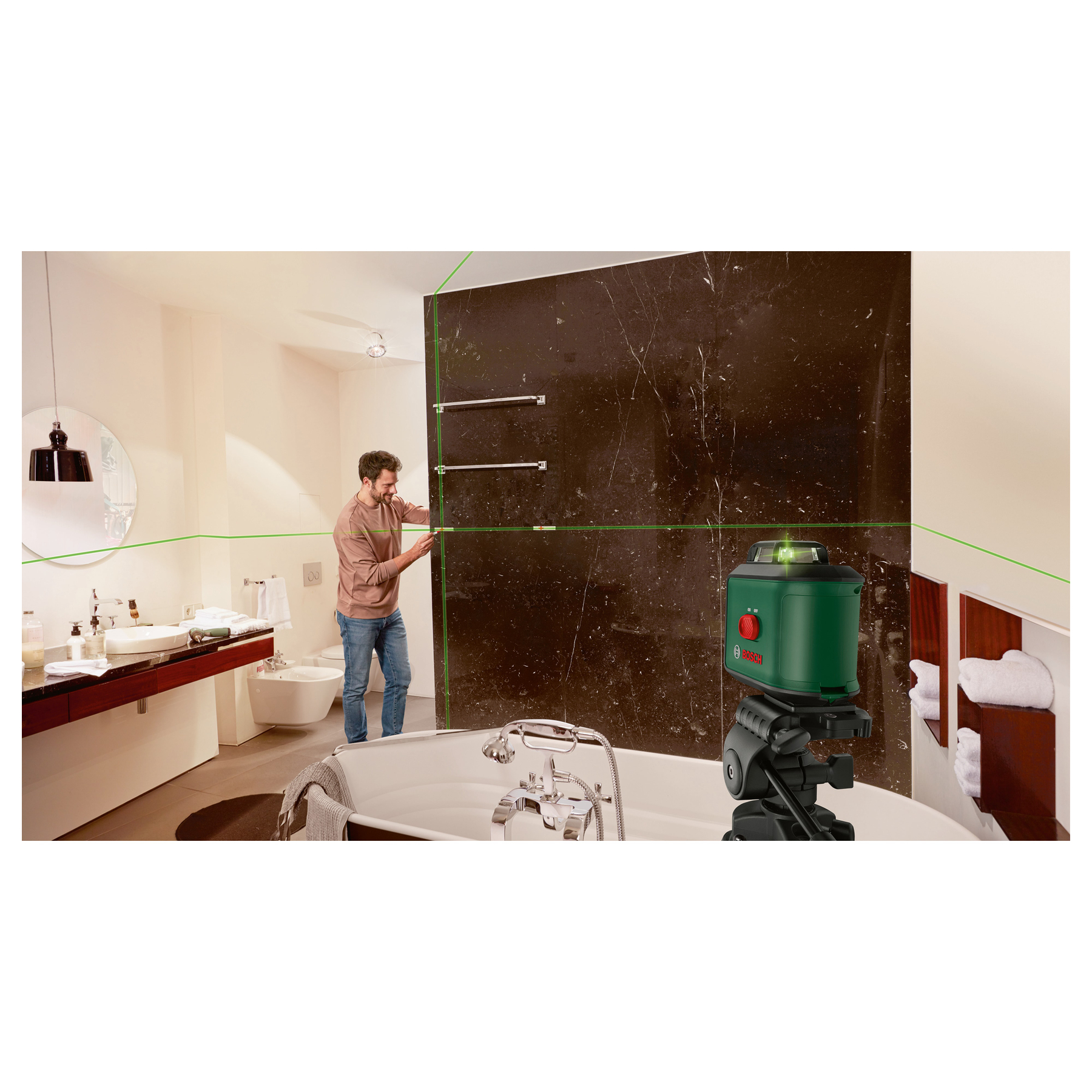 Mężczyzna używa poziomicy laserowej w łazience, sprawdzając wyrównanie. Zielona linia lasera pojawia się na ciemnej ścianie.