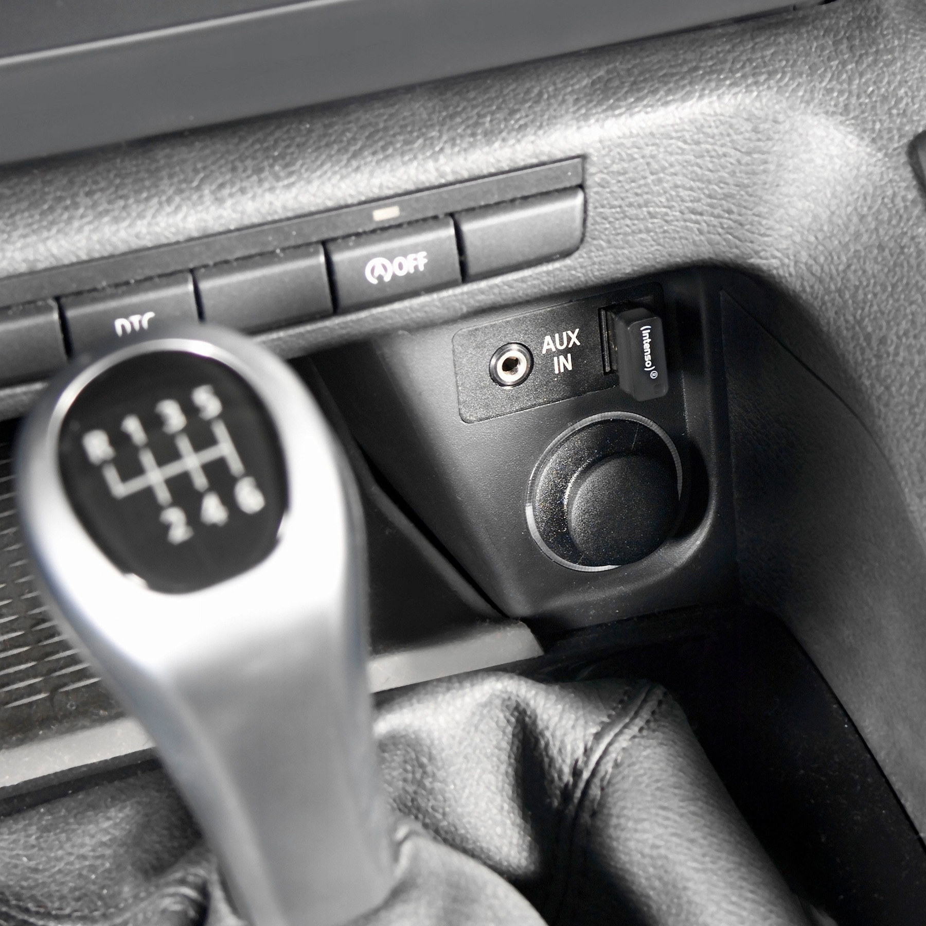 Szczegół wnętrza samochodu. Dźwignia zmiany biegów, wejście aux, gniazdo zasilania i przyciski na czarnej konsoli. Skórzana osłona dźwigni.