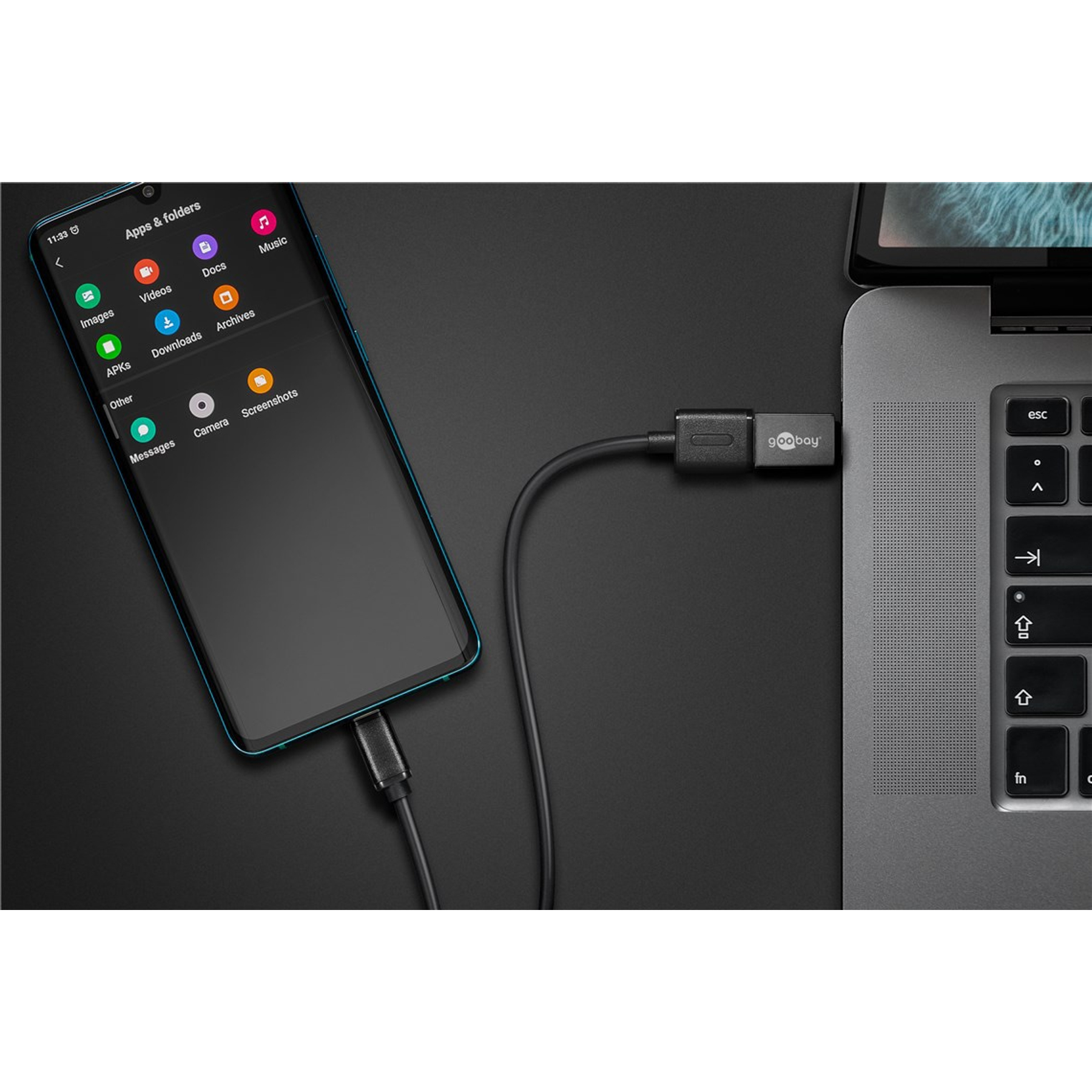 Uno smartphone è collegato a un laptop tramite un cavo nero. Il telefono visualizza le icone delle app. Un adattatore 'goobay' è sul cavo.