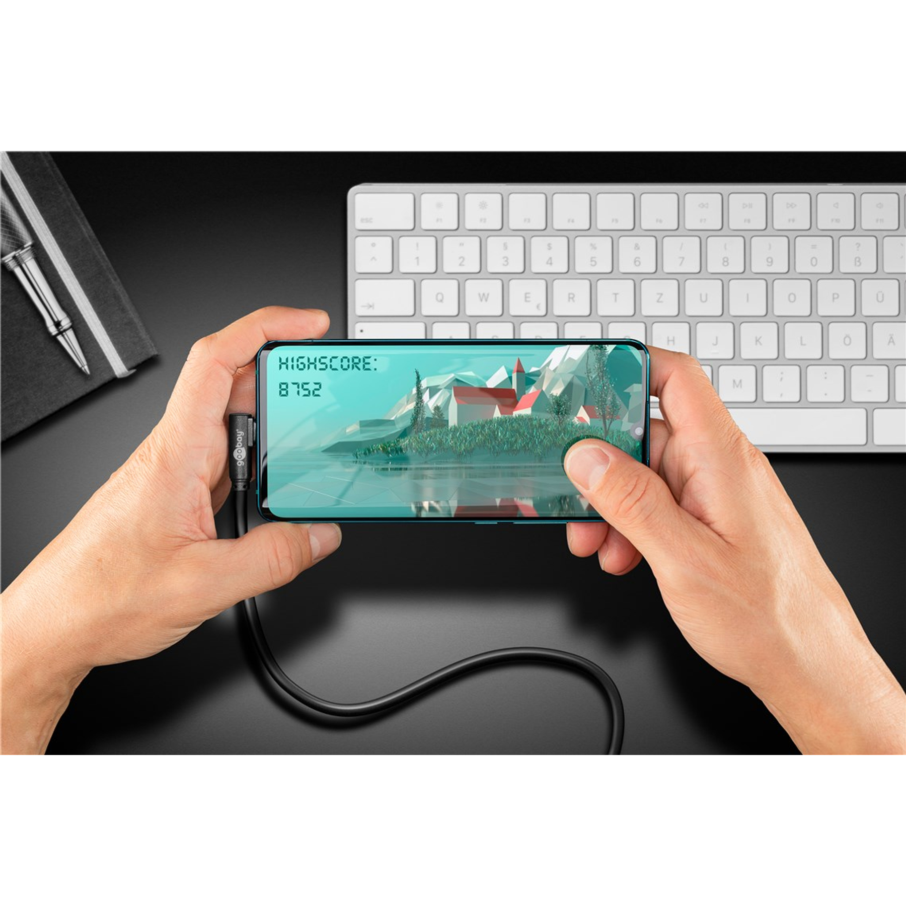 Hands holding a smartphone displaying a game scene with a high score. A keyboard and pen are in the background.