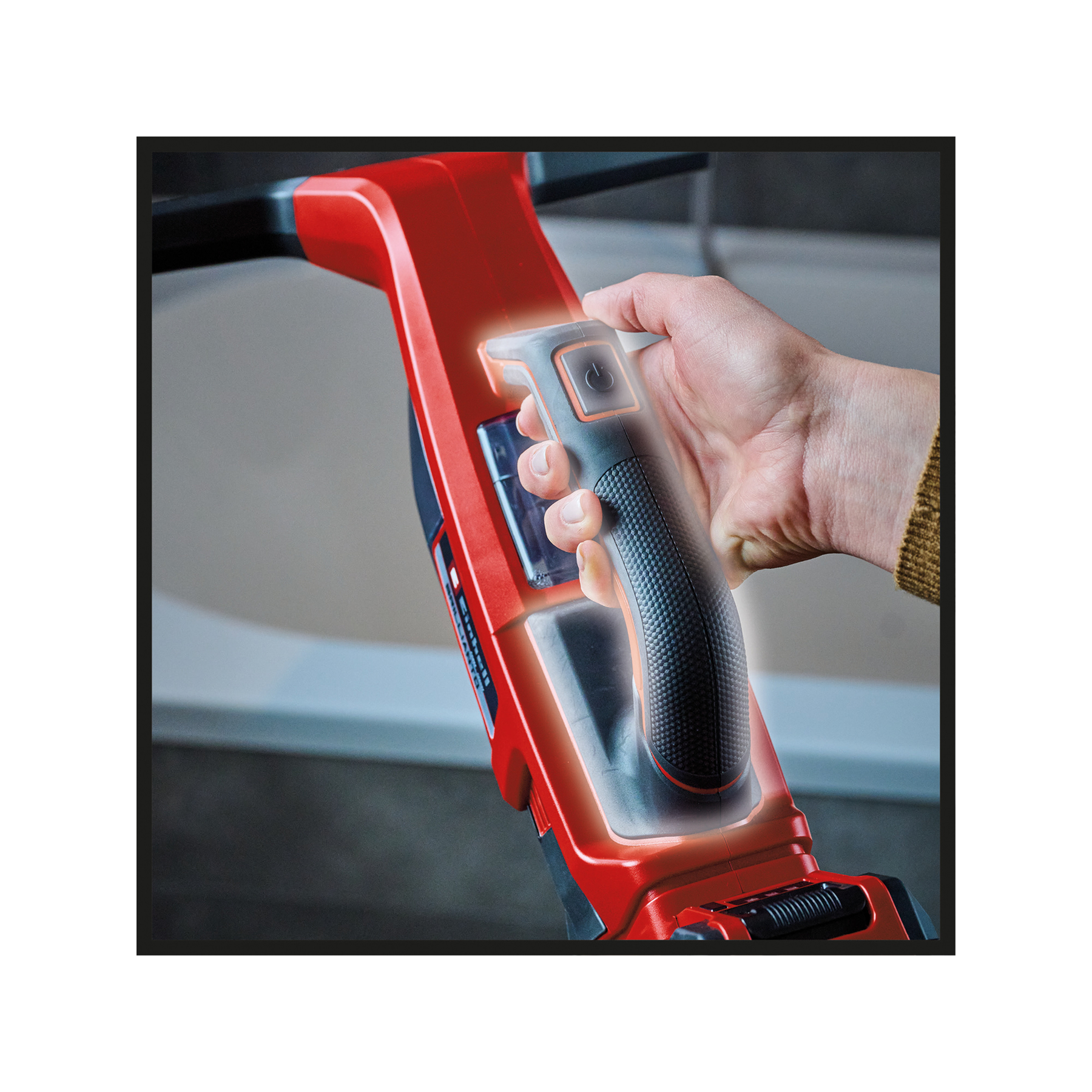 Ręka trzymająca czerwono-czarne narzędzie do czyszczenia. Narzędzie ma przycisk zasilania. Światło świeci wokół uchwytu.