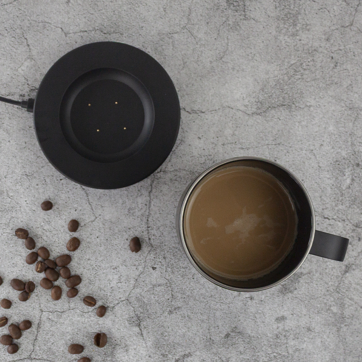 Overhead view: coffee mug with coffee, black warmer, coffee beans on gray textured surface.