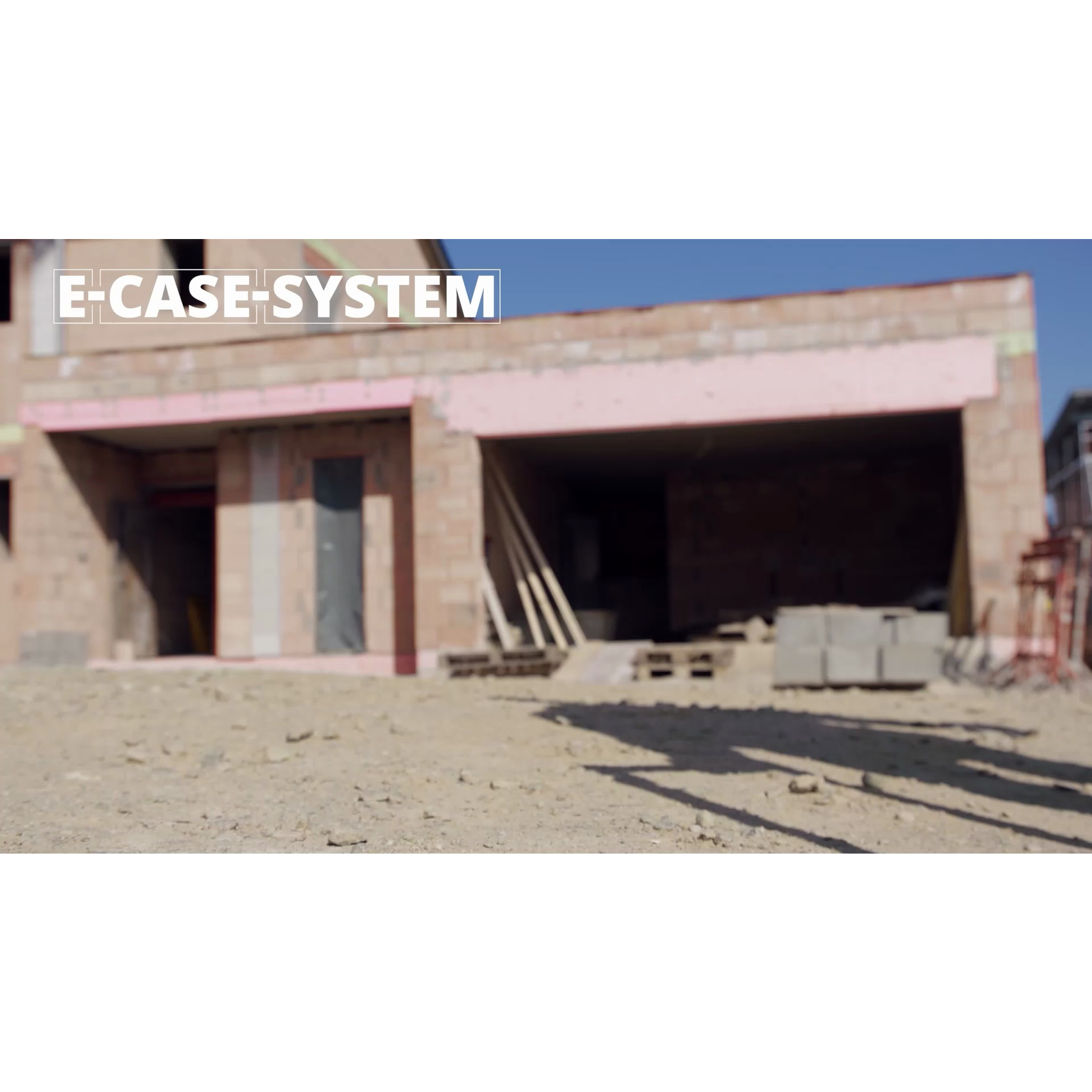 Baustelle mit freiliegender Ziegelstruktur, sichtbaren Garagenöffnungen und Text "E-CASE-SYSTEM" oben. Sonnig, tagsüber.