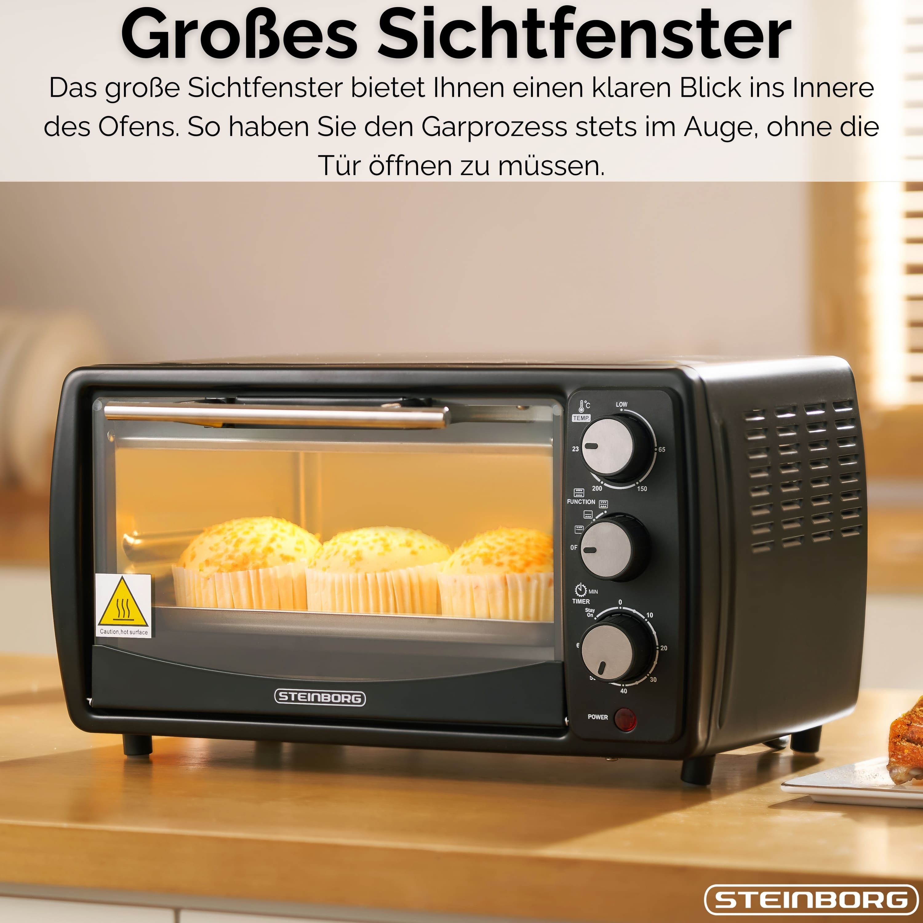 Ein schwarzer Ofen mit drei Muffins. Bedienelemente vorne. Der Ofen steht auf einer Holzoberfläche.
