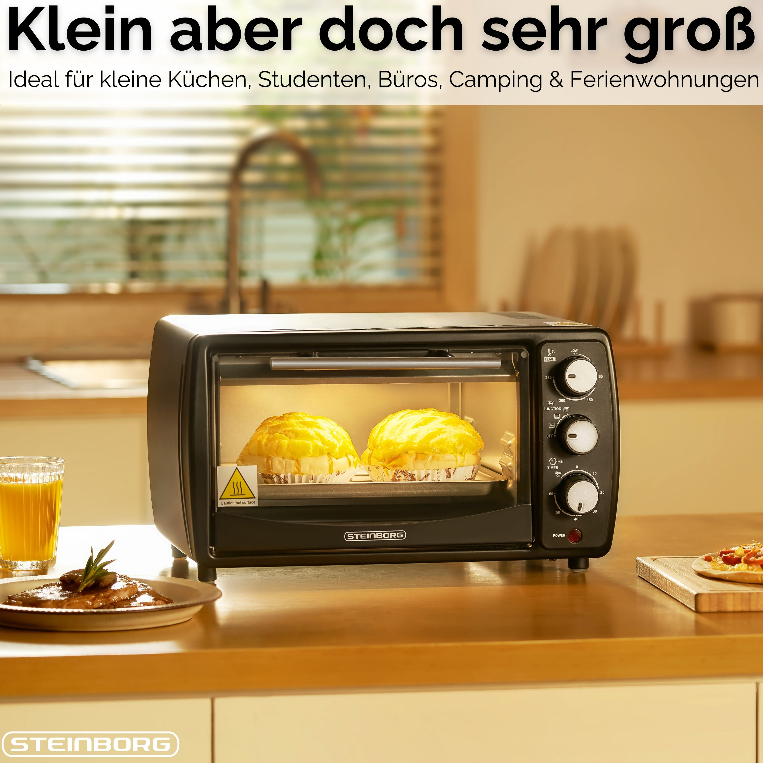 Ein schwarzer Steinborg-Ofen mit zwei darin backenden Brötchen. Ein Glas Saft, ein Teller mit Essen und eine Pizza.