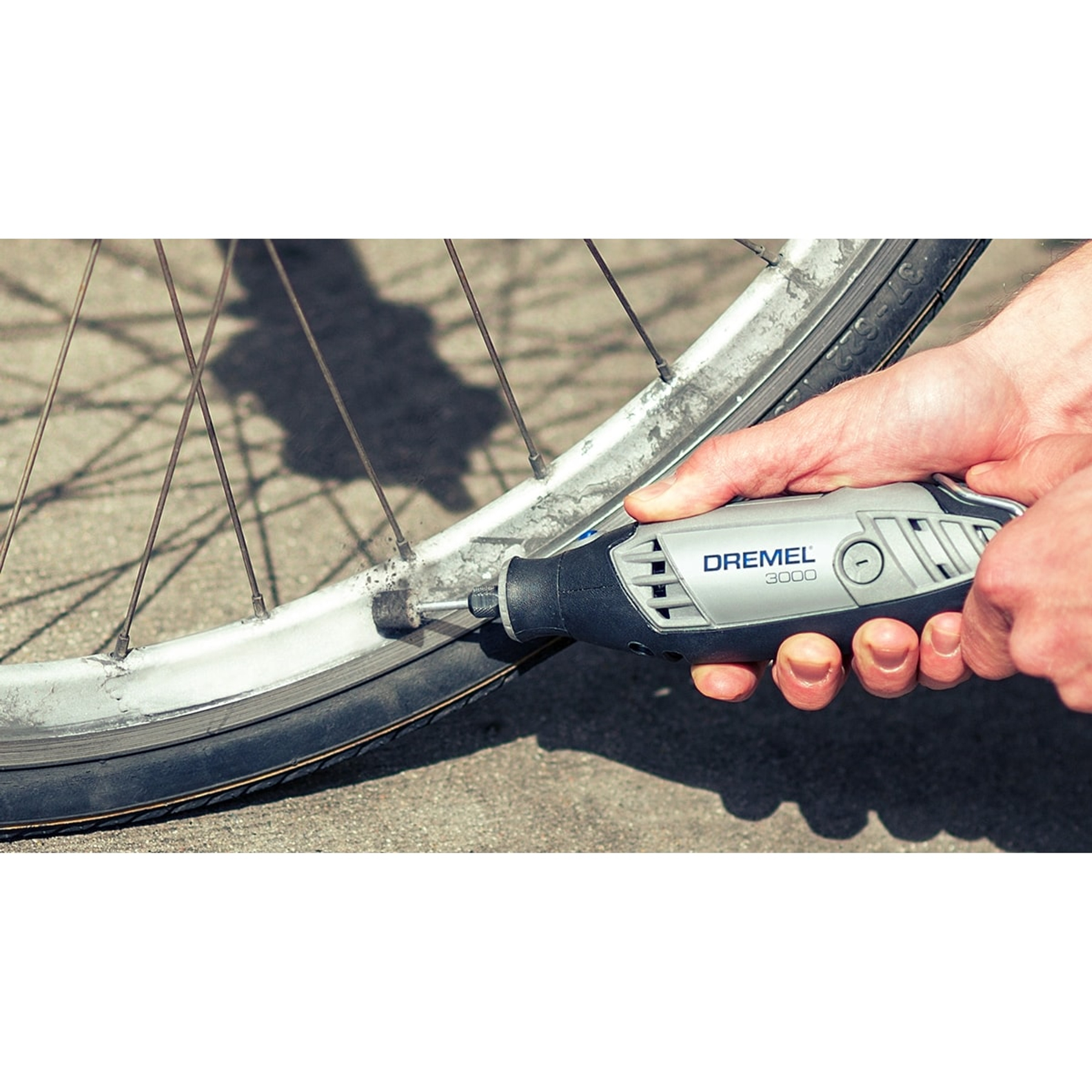 Eine Hand reinigt mit einem Dremel-Werkzeug ein Fahrradrad. Das Rad ist verschmutzt, das Werkzeug grau und schwarz.