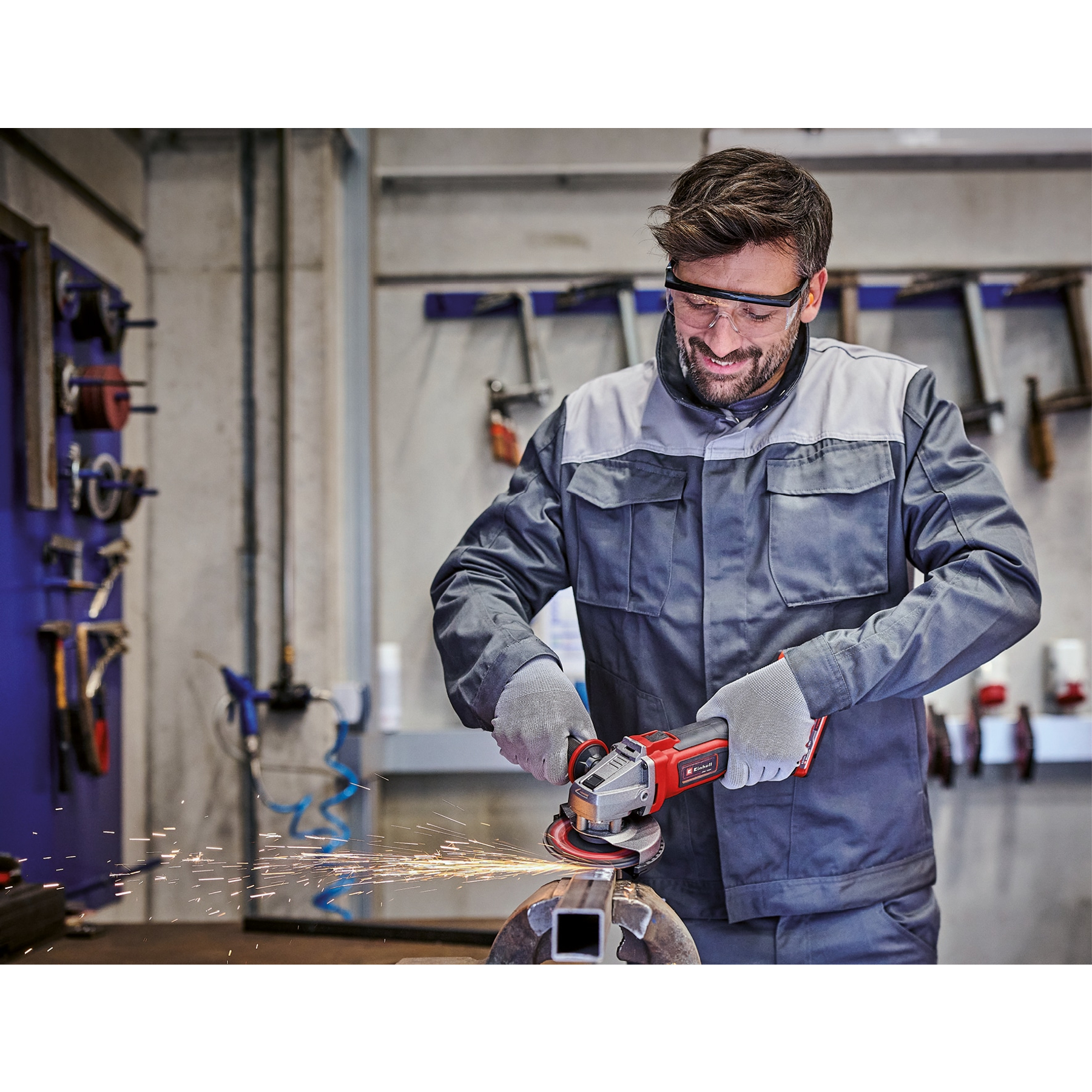 Mężczyzna szlifuje metal szlifierką kątową, w okularach i rękawicach ochronnych, w warsztacie. Iskry lecą.
