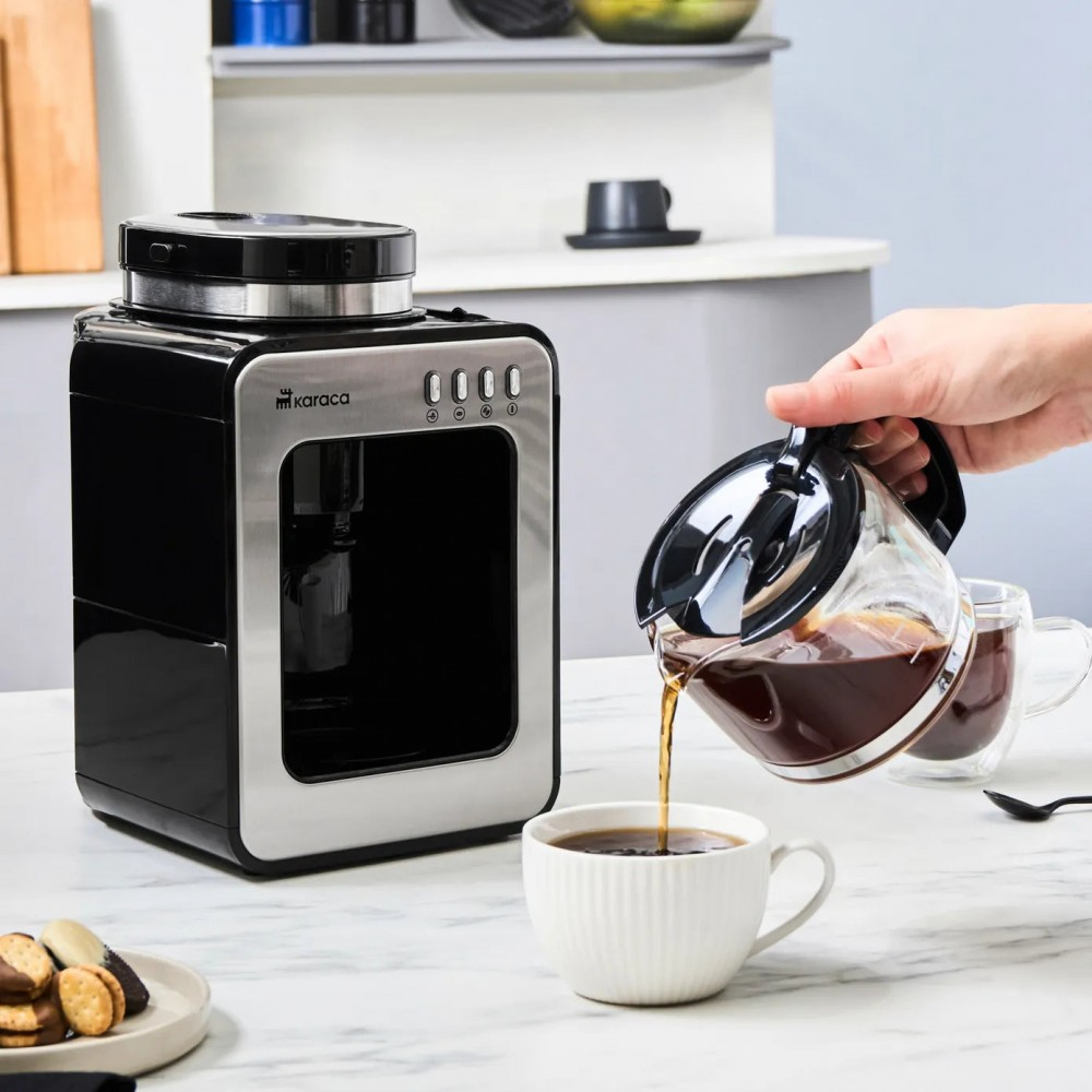 Una persona versa caffè da una caraffa di vetro in una tazza bianca. Una macchina da caffè a sinistra. Biscotti su un piatto.