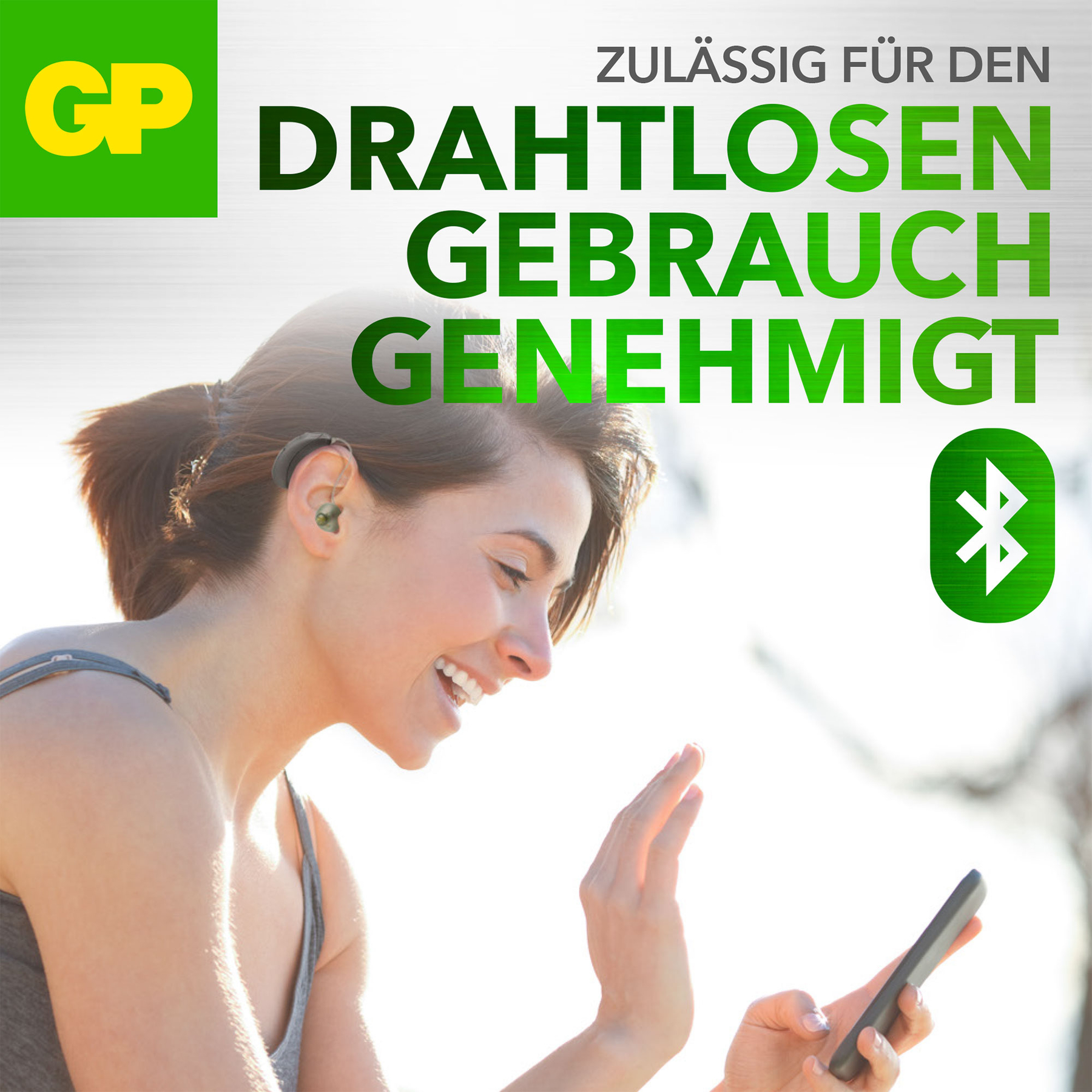 Donna sorridente con apparecchio acustico, tiene un telefono. Testo verde in tedesco dice 'approvato per l'uso wireless'.