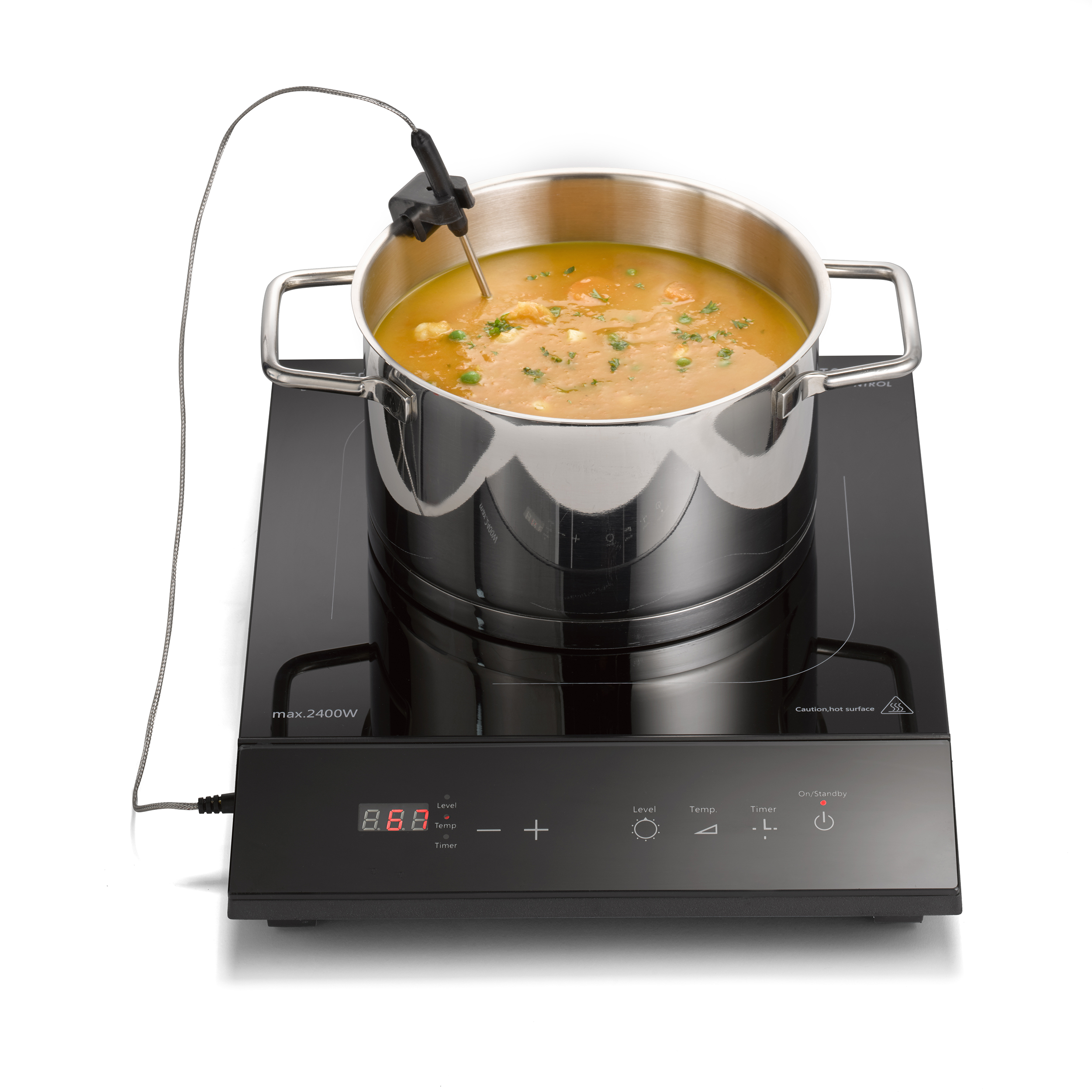 Una pentola di zuppa con un termometro su un piano cottura a induzione nero. La zuppa ha piselli e carote.