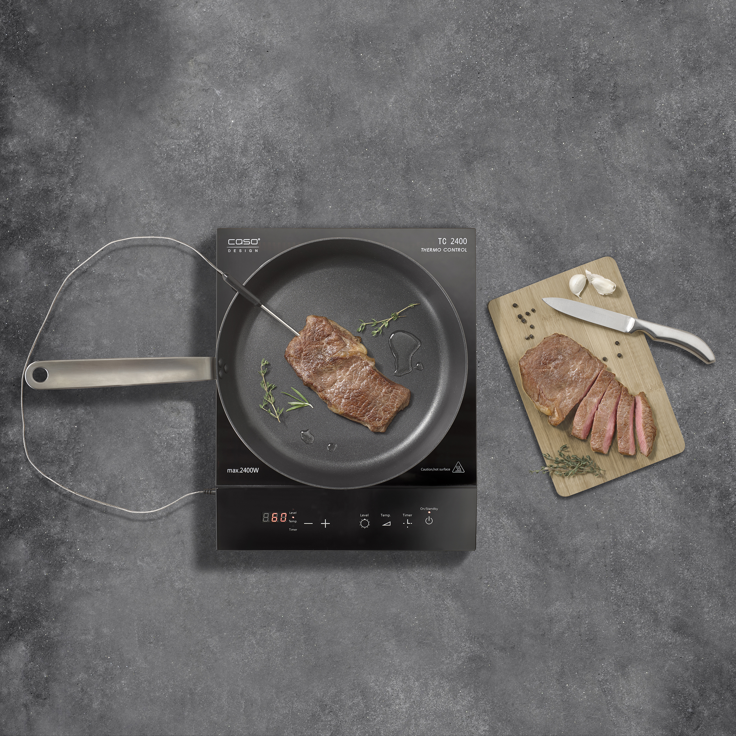 Una bistecca cuoce in padella su un piano a induzione. Tagliere con bistecca a fette, aglio e coltello.