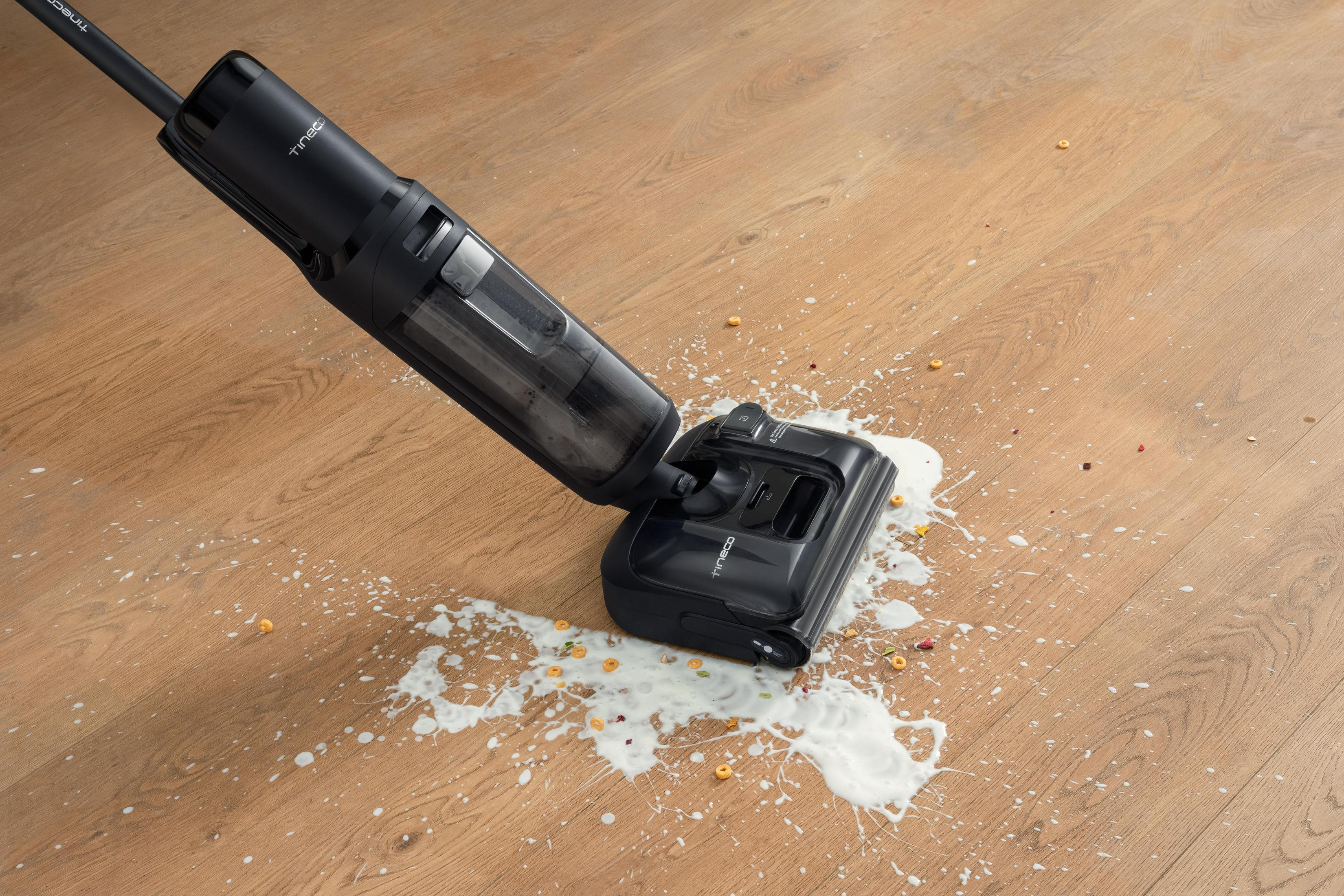 Czarny odkurzacz na drewnianej podłodze, czyszczący rozlane mleko, płatki i inne zanieczyszczenia.