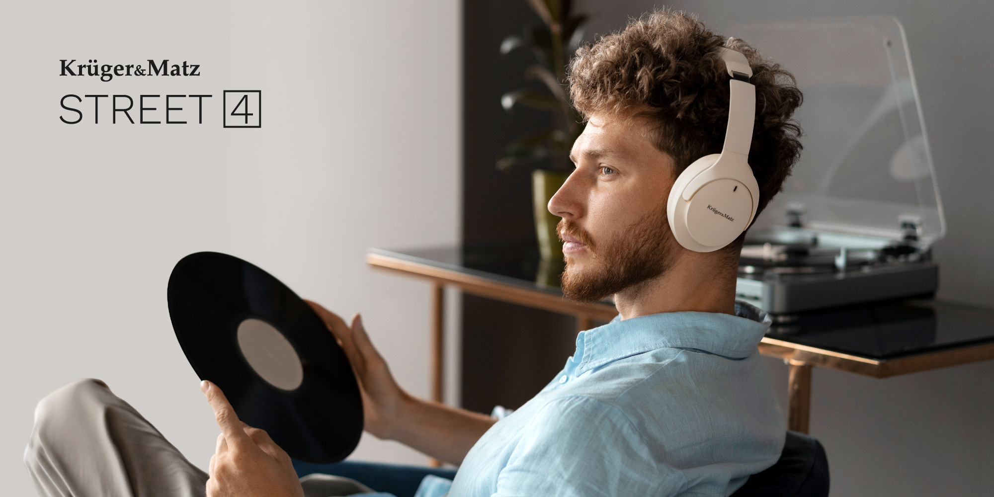 Mężczyzna ze słuchawkami trzyma płytę winylową. W tle gramofon. Widoczna nazwa marki.