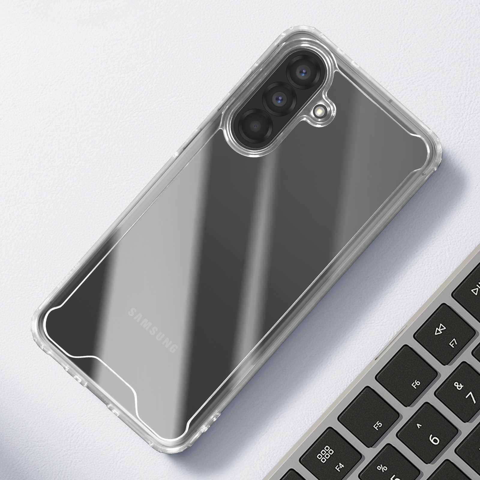 Une coque de téléphone transparente avec un téléphone Samsung à l'intérieur, posée sur une surface blanche. Un clavier est partiellement visible à droite.