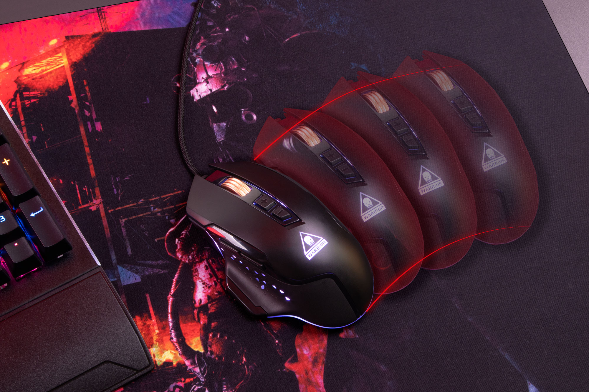 Czarna mysz do gier z czerwonymi akcentami, umieszczona na podkładce. Klawiatura w rogu. Widoczne słowo "WARRIOR".