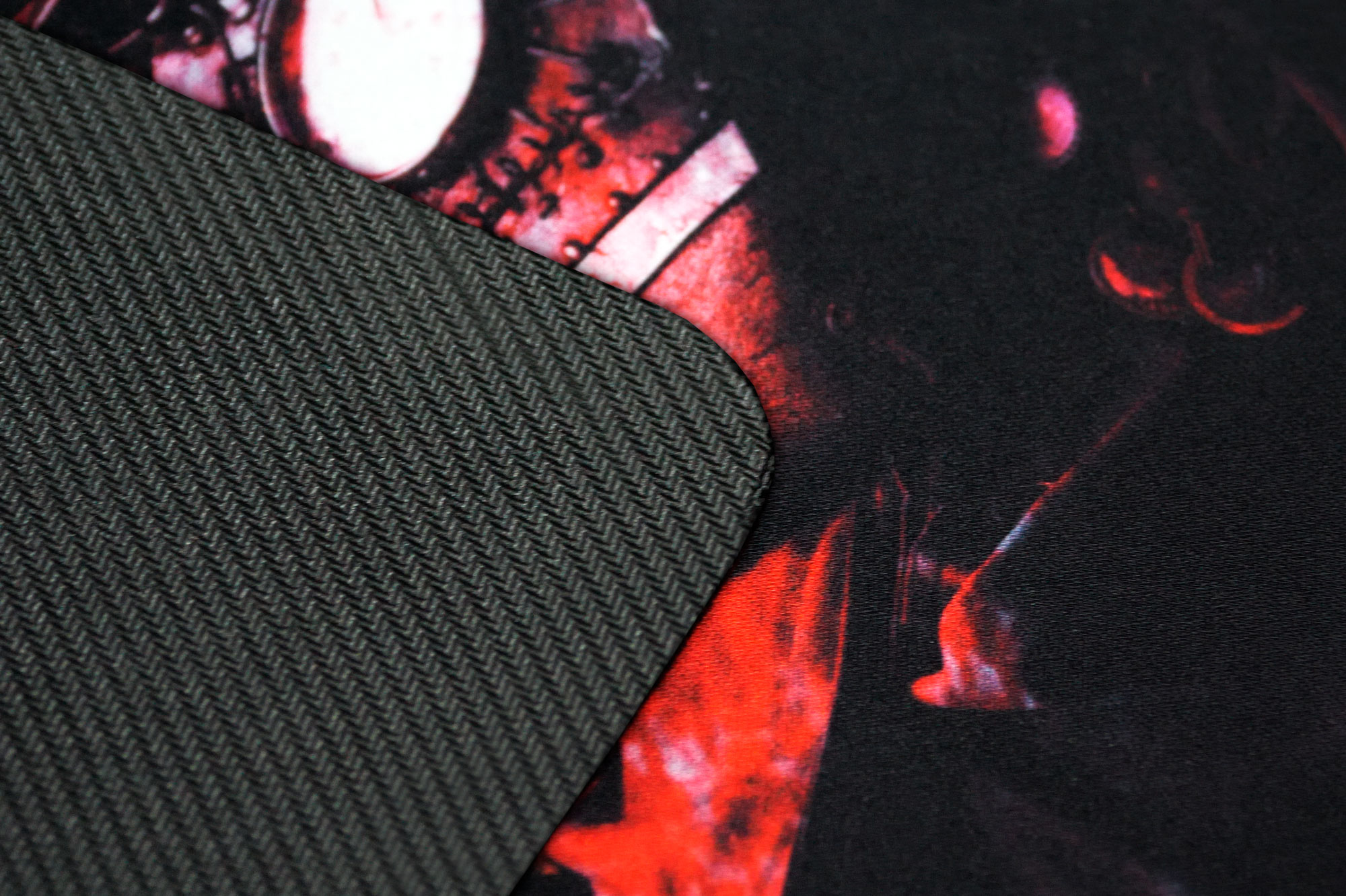 Zbliżenie czarnej podkładki pod mysz z teksturowaną powierzchnią. Część podkładki ma czerwono-czarną grafikę. Druga część jest szara.