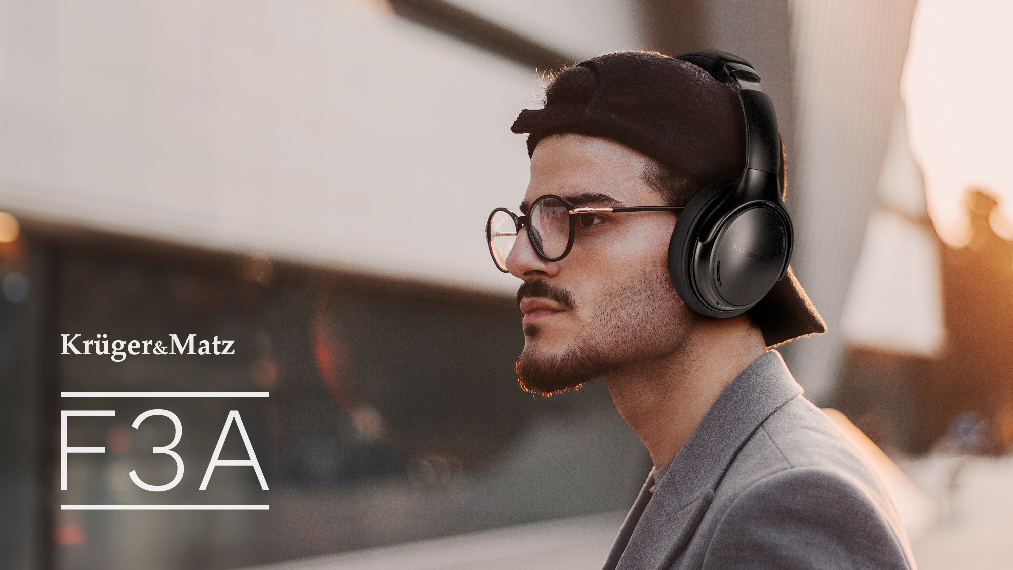 Mężczyzna w okularach i słuchawkach, patrzący w bok. Obraz ma ciepły ton, widoczne logo.