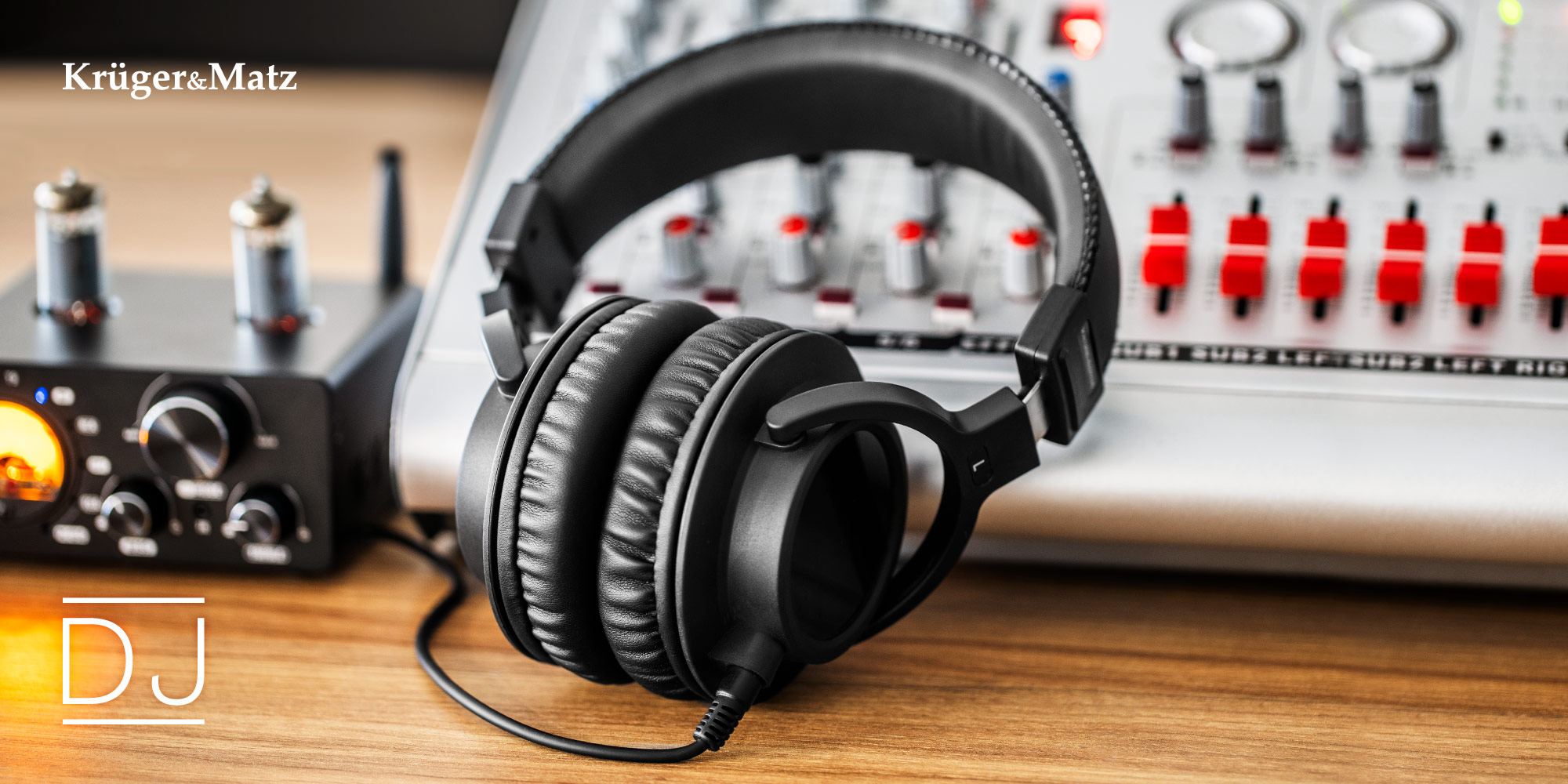 Czarne słuchawki na drewnianym biurku z mikserem w tle. Logo DJ w lewym dolnym rogu.
